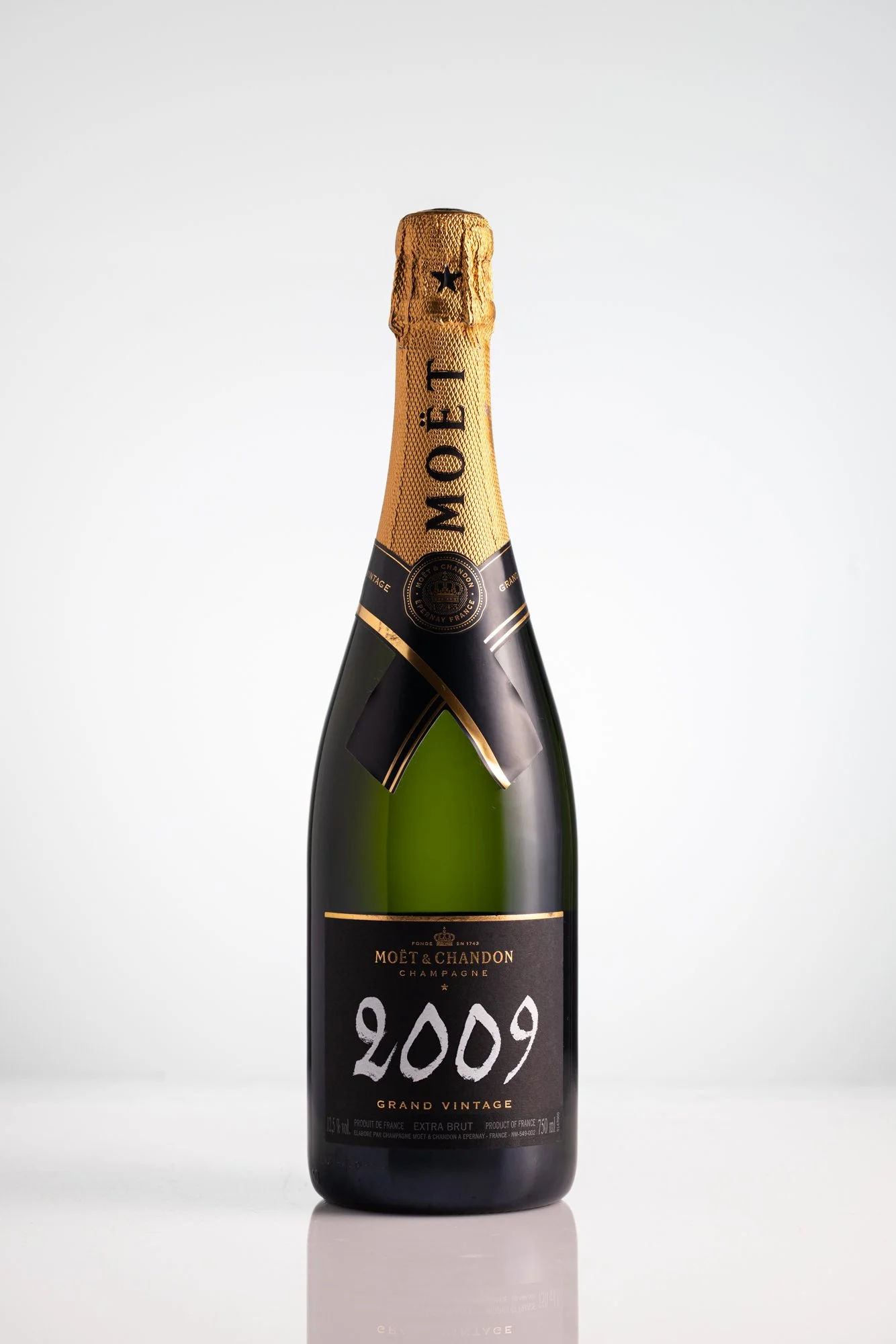 A bottle of Moët & Chandon Grand Vintage champagne from 2009 with a black label and gold accents, standing on a reflective surface against a plain light gray background. product photography