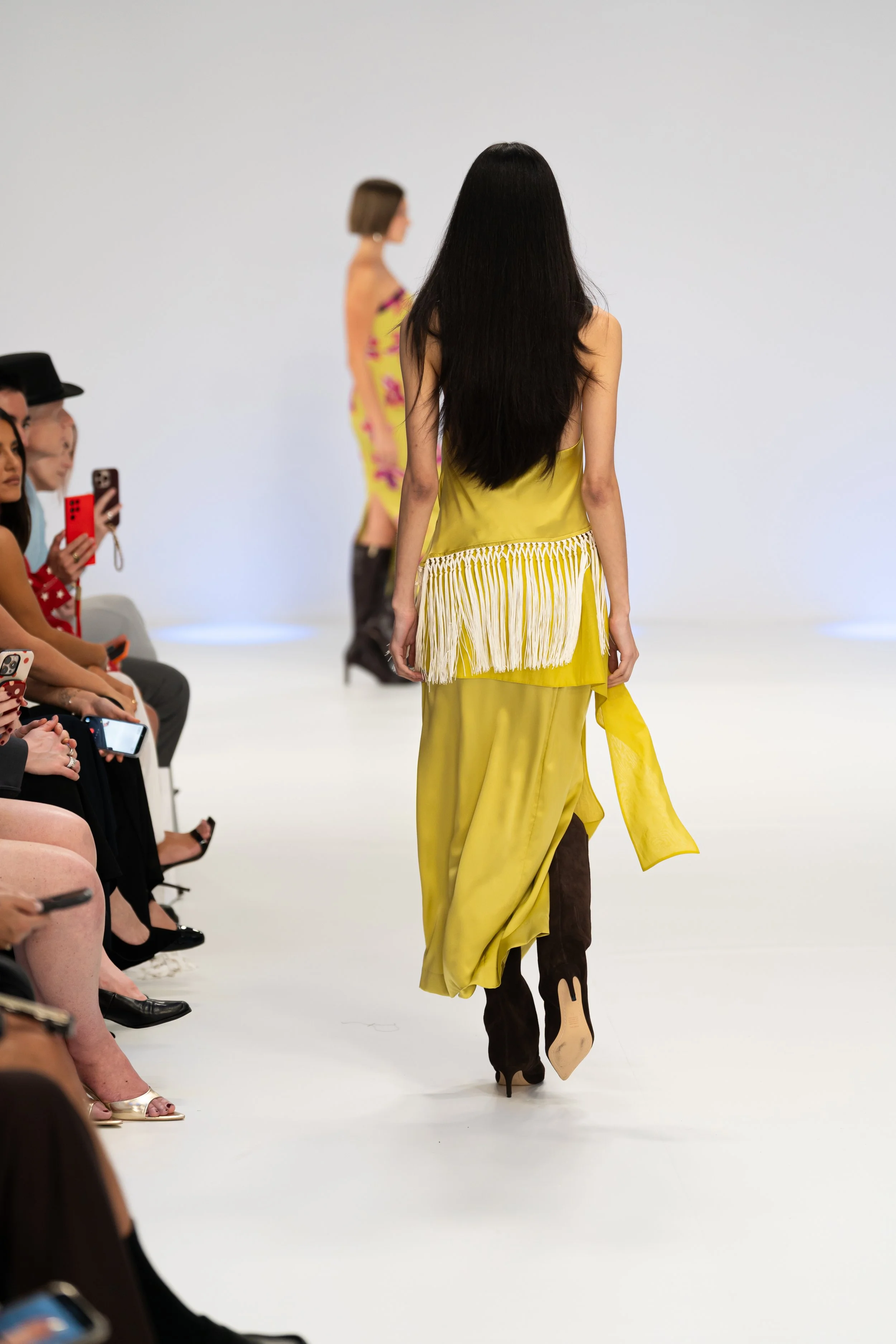 Models walk down the runway at a fashion show while sitting audience members take photos. silk laundry runway show at Australian fashion week 2026 the edit runway