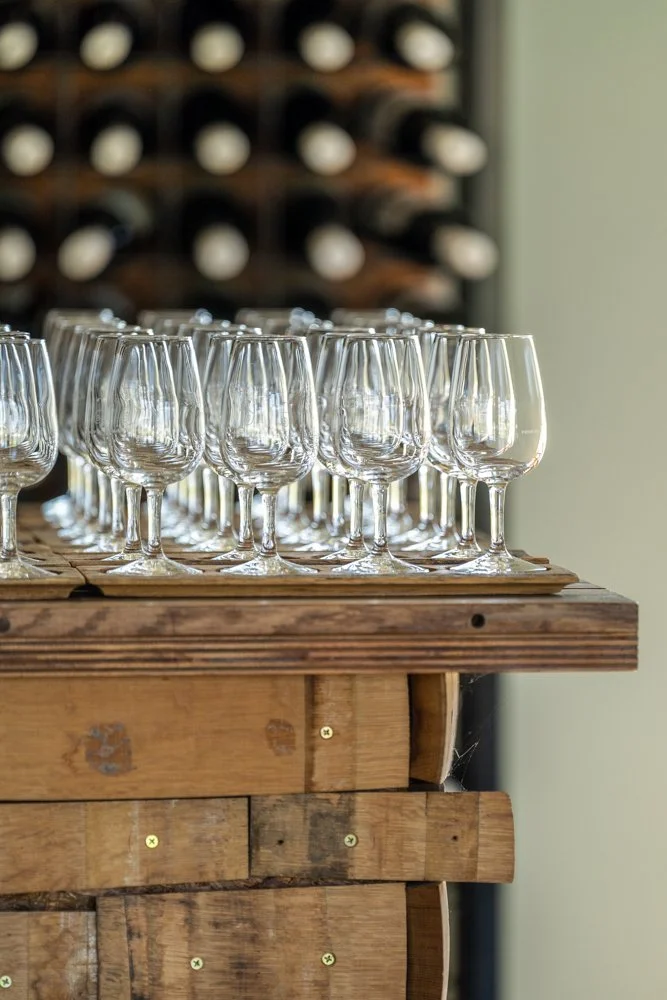 Multiple empty wine glasses on a wooden table with a wine rack in the background. four winds vineyards