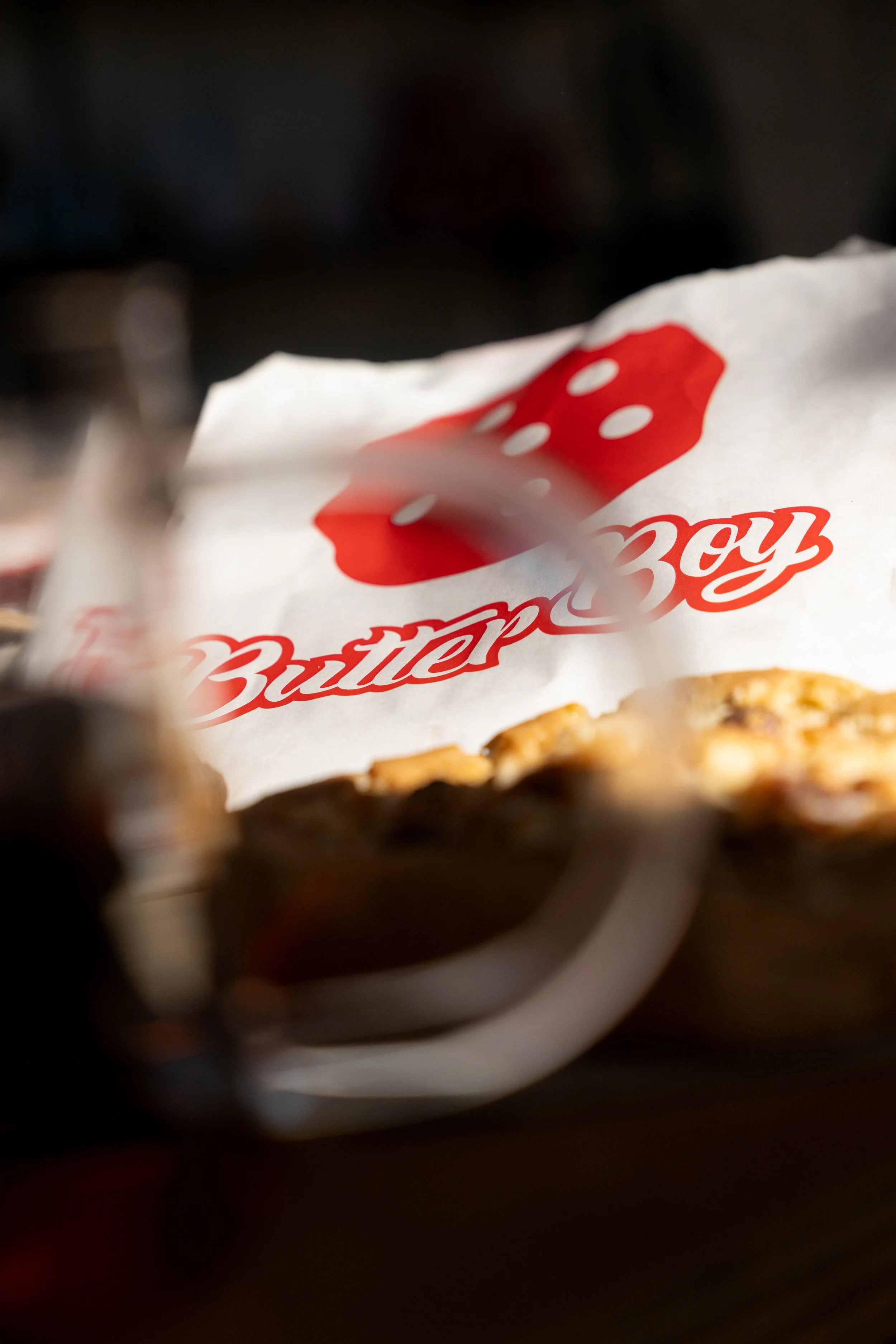 Close-up of a crumpled white paper bag with red text and a die symbol printed on it. butter boy cookie at redbrick cafe in curtin 
