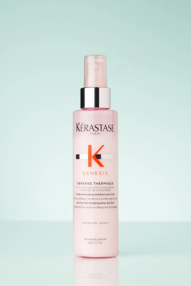 Pink spray bottle of Kerastase Genesis anti-hair fall fortifying blow-dry fluid against a light green background. product photography