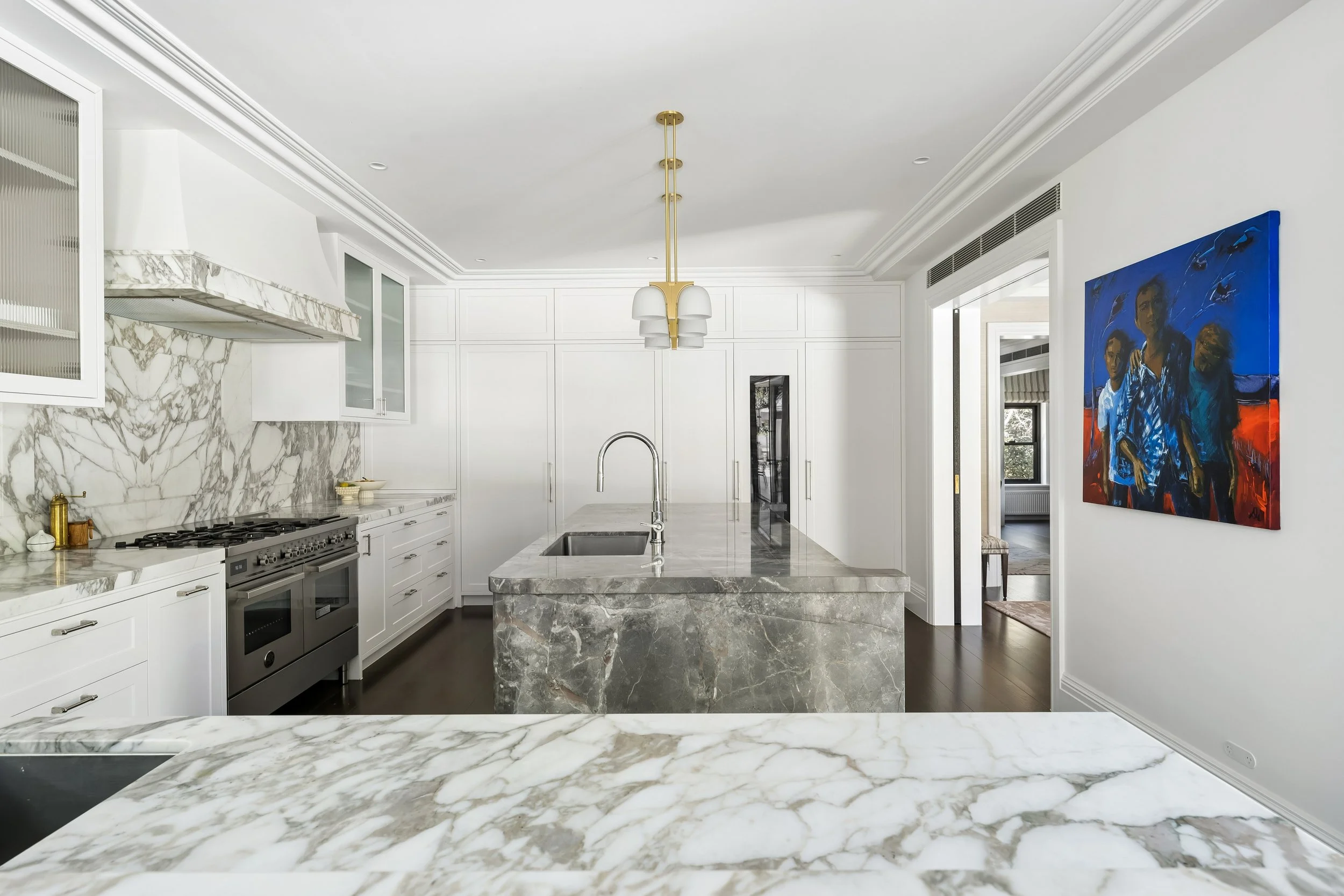 Modern kitchen with white cabinets, marble countertops, a central marble island, and a colorful portrait painting on the wall. architectural photography for thursday architecture in canberra australia - magazine editorial photography designer kitchen