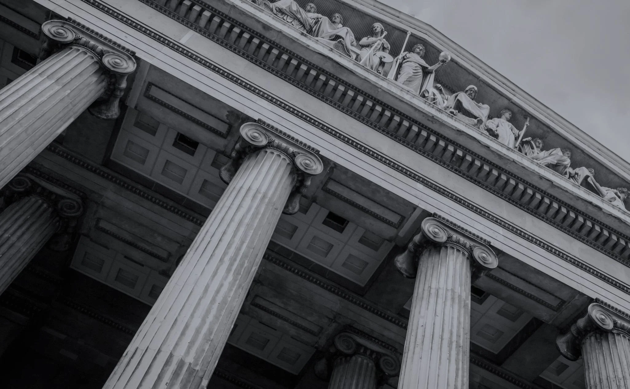 Close-up of a classical building facade with tall, fluted columns topped by ornate capitals. The building features sculpted statues and detailed architectural elements in black and white.