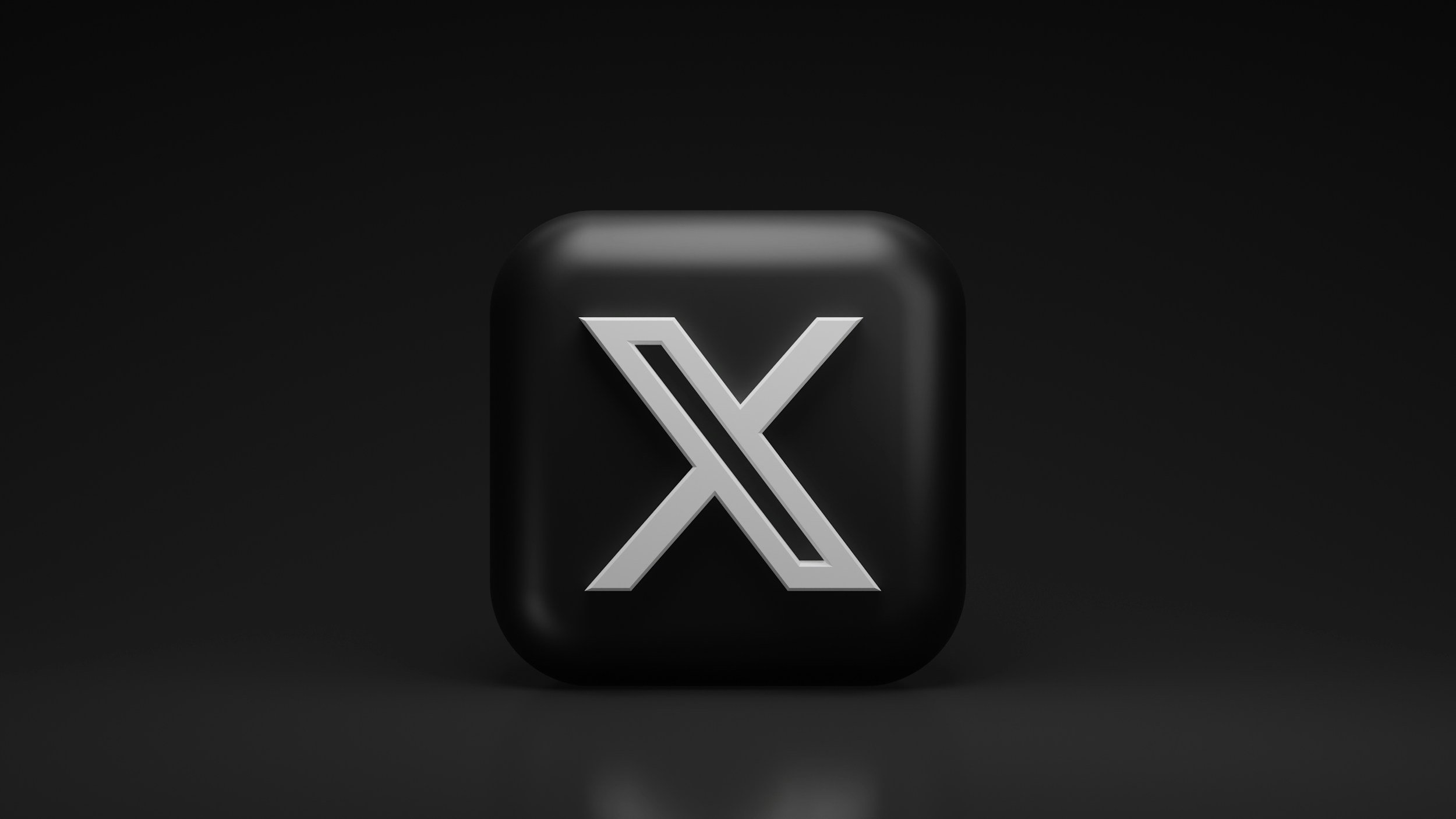 A black and gray icon with a stylized letter 'X' in the center, set against a dark background.
