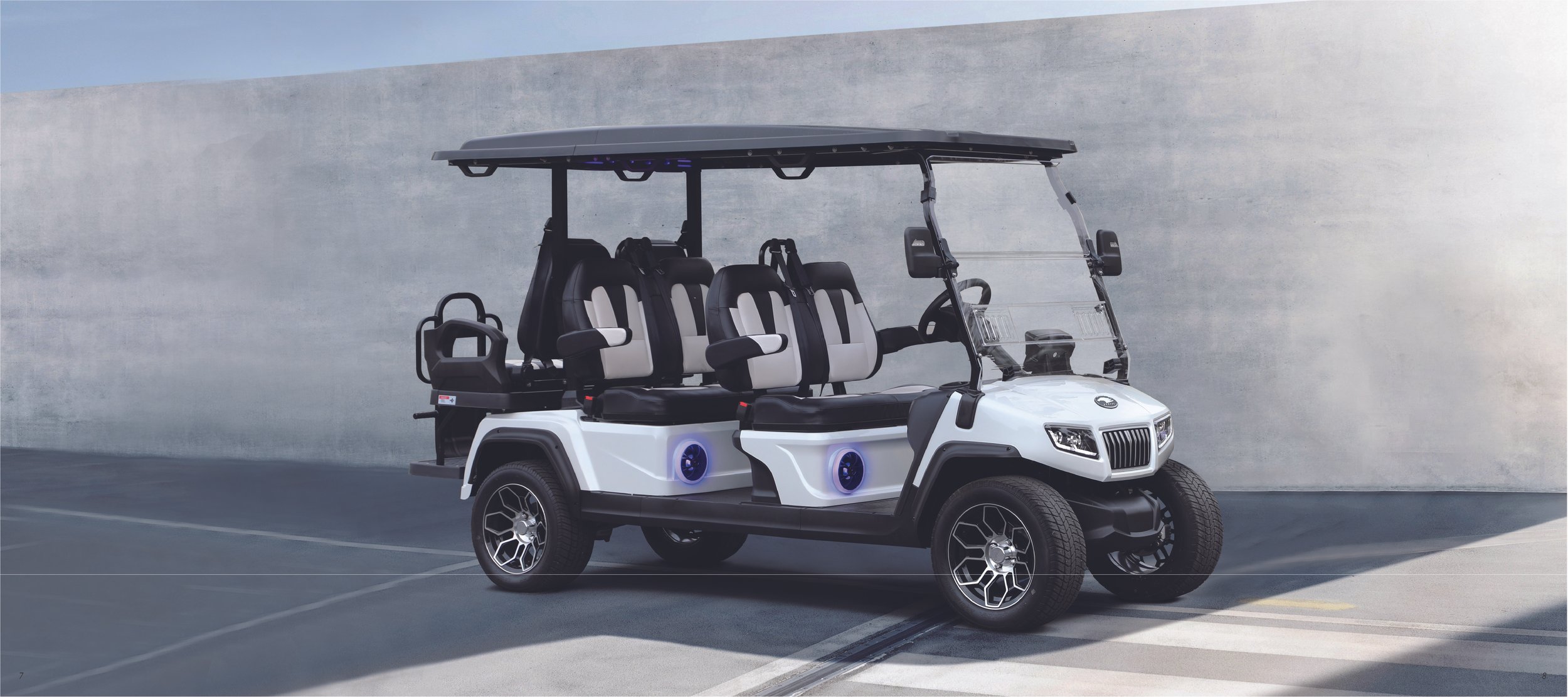 A white electric golf cart with four rows of seats, two seats in the front and three in the back, parked against a concrete wall.