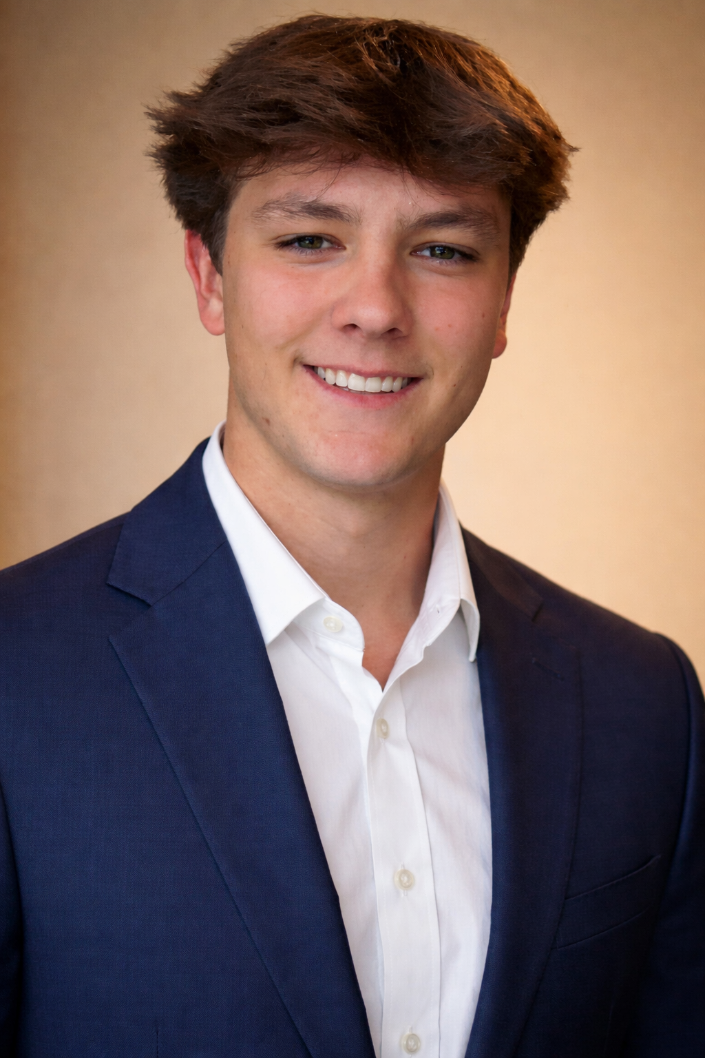 A young man in a dark suit and white shirt smiling at the camera.