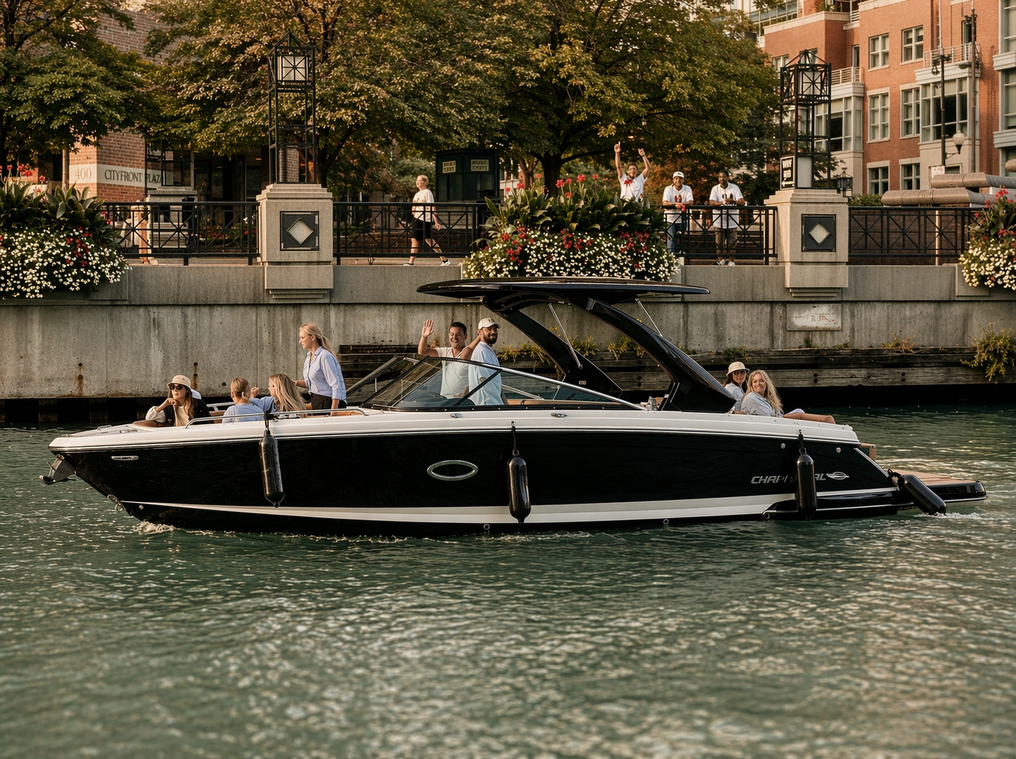 A black and white motor boat with people onboard, sailing on a river with a cityscape background. Some individuals are waving, and others are relaxing, with a bridge and buildings, trees, project details, and flowers visible in the scene.