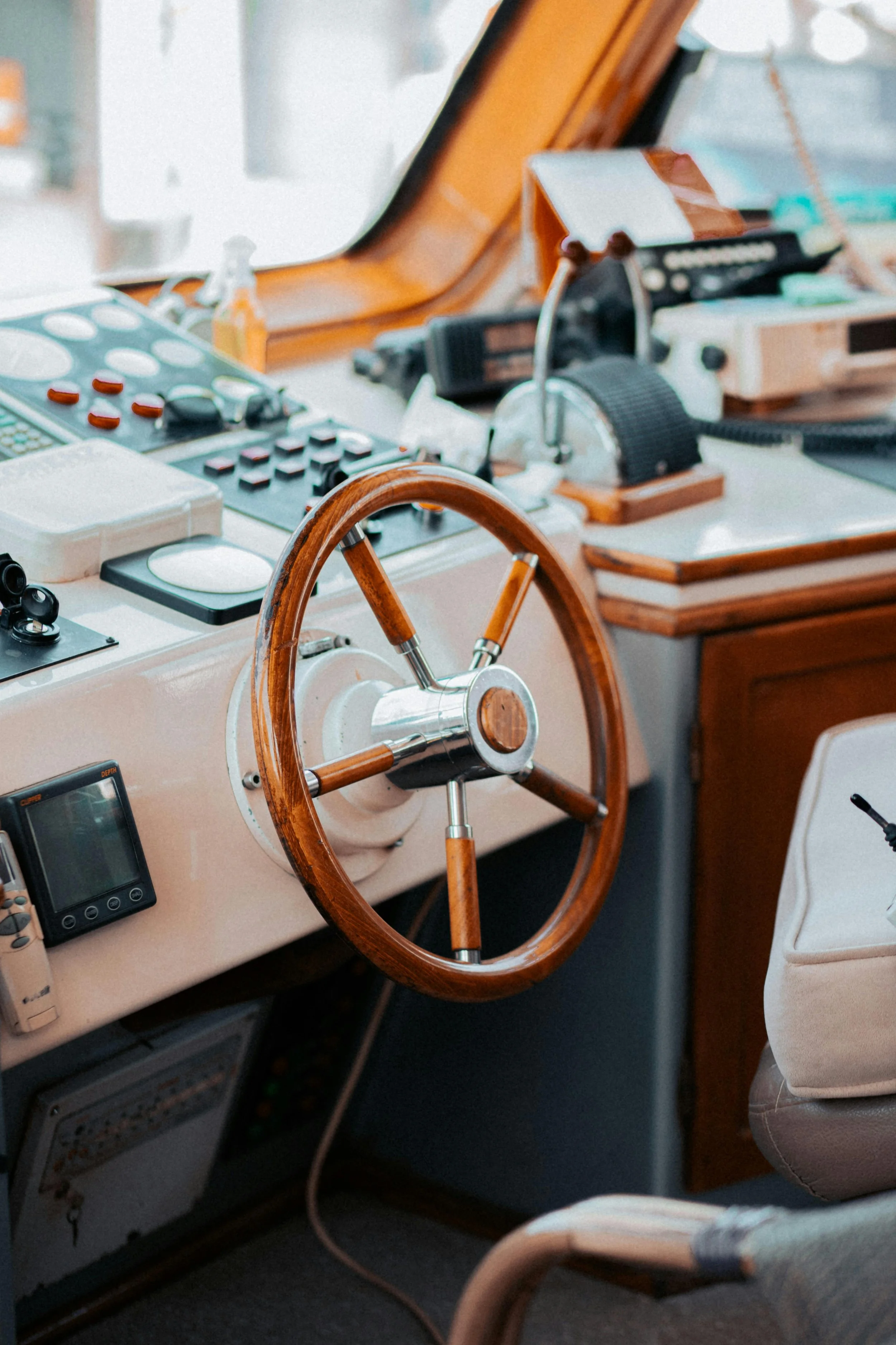 Close-up of a boat's dashboard and steering wheel, with navigational and communication equipment, and a chair nearby.
