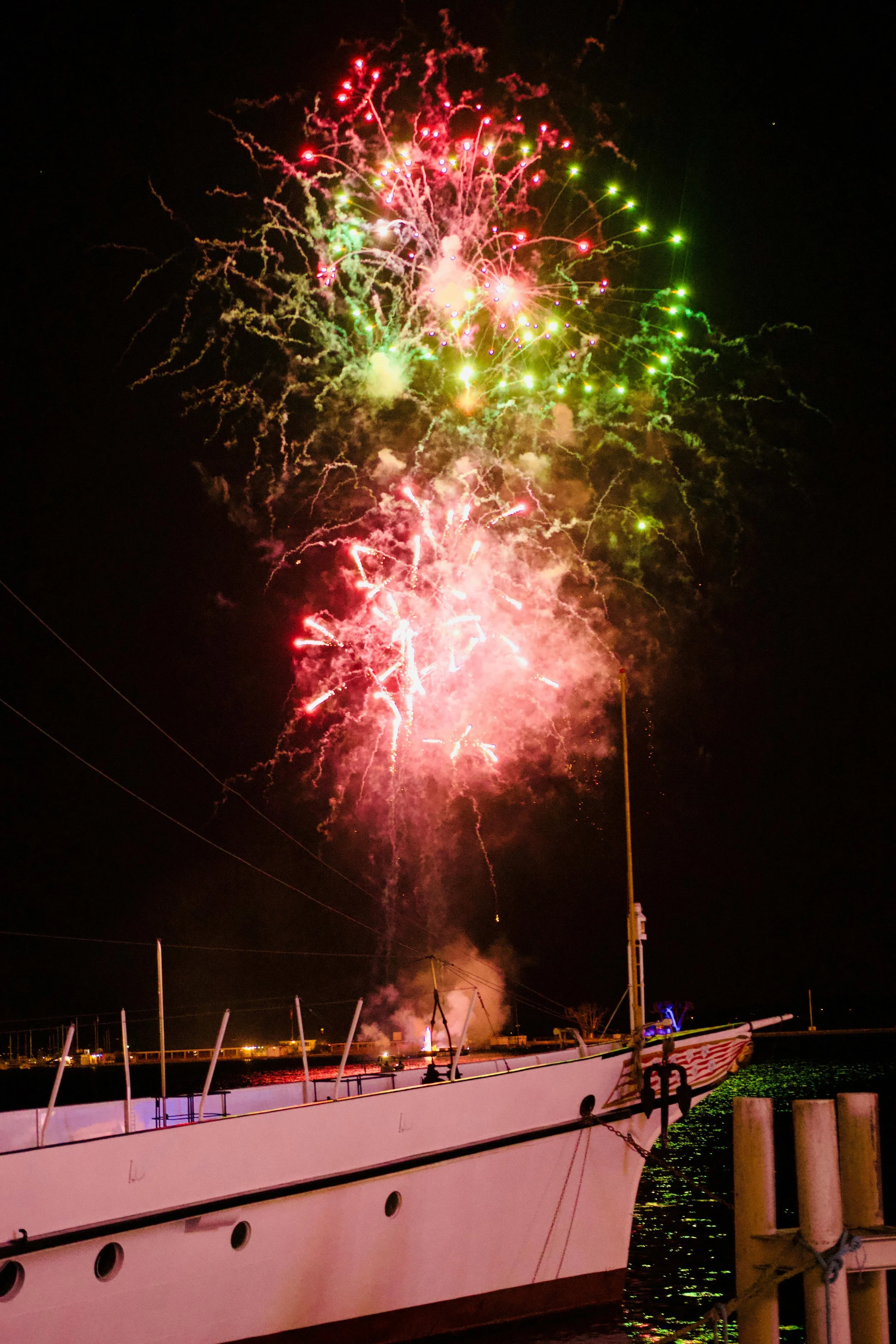 Colorful fireworks lighting up the night sky over a docked boat at a marina.