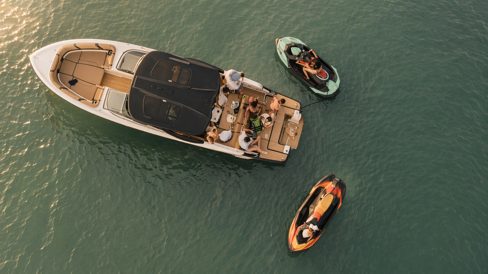 Overhead view of a yacht with people on deck and two smaller boats nearby on the water.