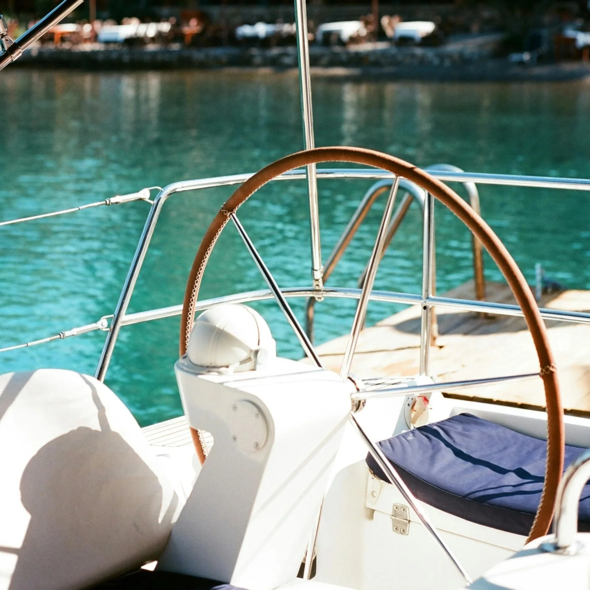 Close-up of white lounge chairs on a boat deck with a view of calm water and a distant shoreline with some buildings and trees.