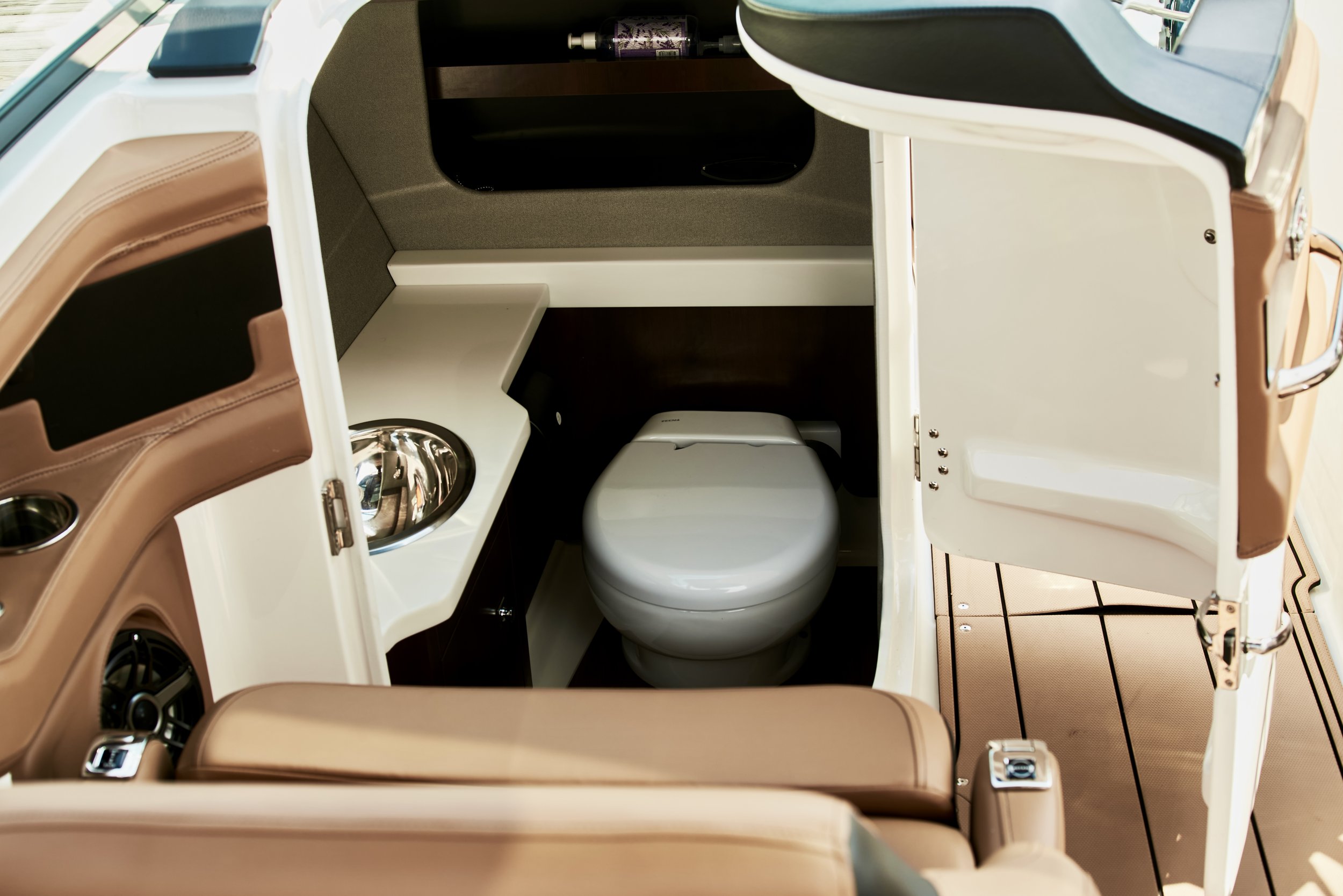Interior of a miniature golf cart with beige cushioned seats, a small stainless steel sink, and a toilet.