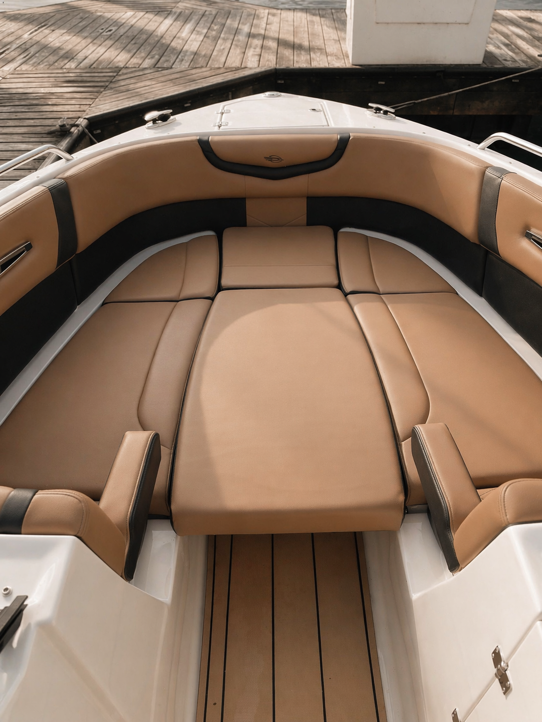 The image shows the interior seating area of a boat with tan and black cushioned seats arranged in a U-shape. The boat is docked, with wooden decking and a white planter visible outside.