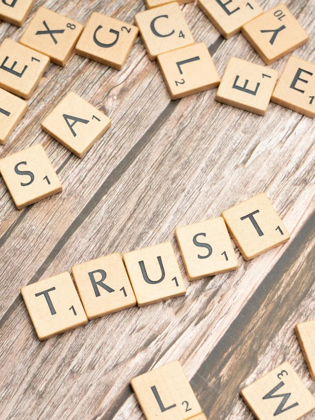 Scrabble tiles arranged to spell out the words "TRUST" and "TRUST" on a wooden surface.