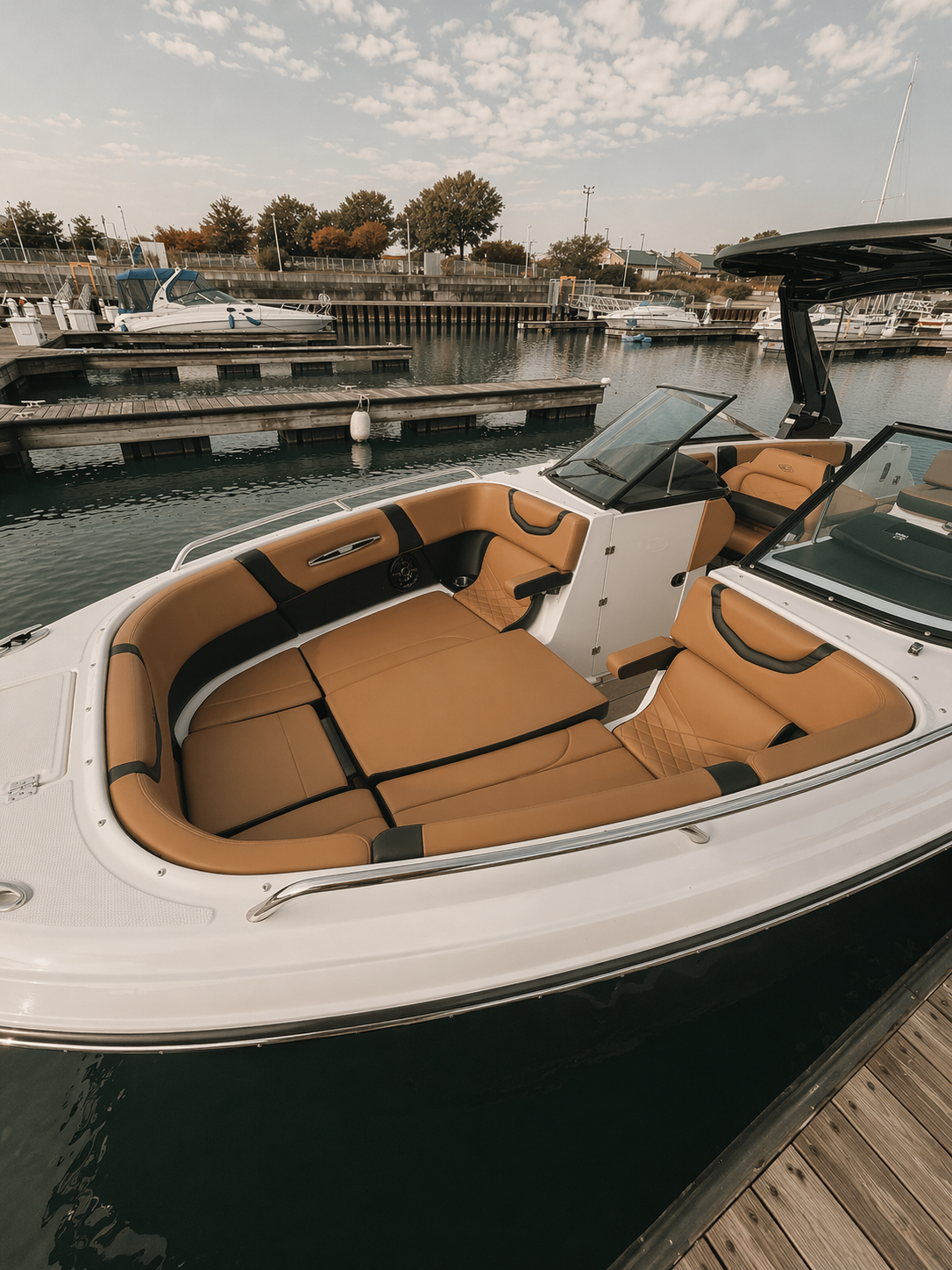 A luxury motorboat docked at a marina with other boats and boats on the water in the background under a partly cloudy sky.
