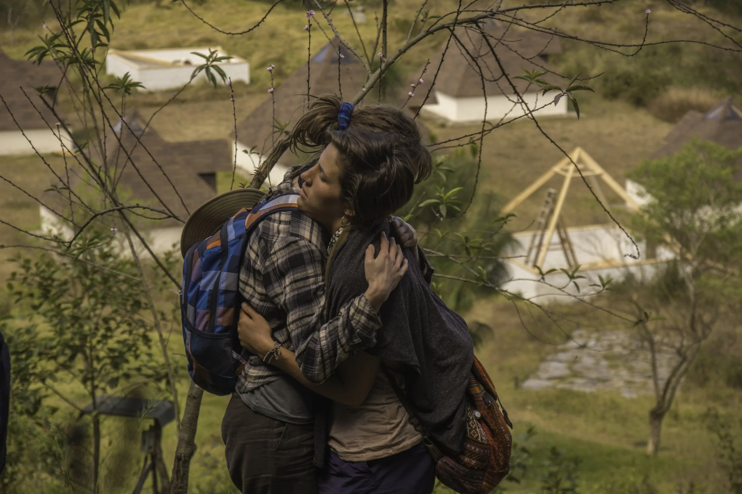 Una pareja abrazada en un árbol, con un fondo de casas y un parque en un entorno natural.