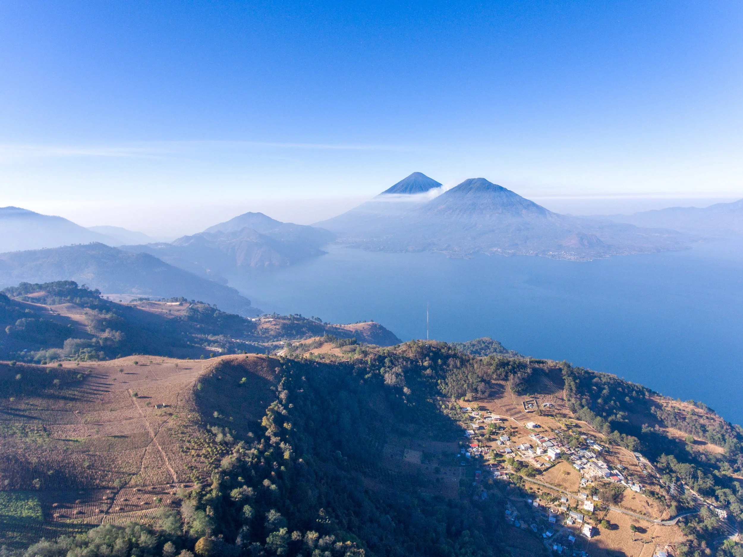 Paisaje con volcanes, agricultura y pequeñas casas en las colinas bajo un cielo despejado.