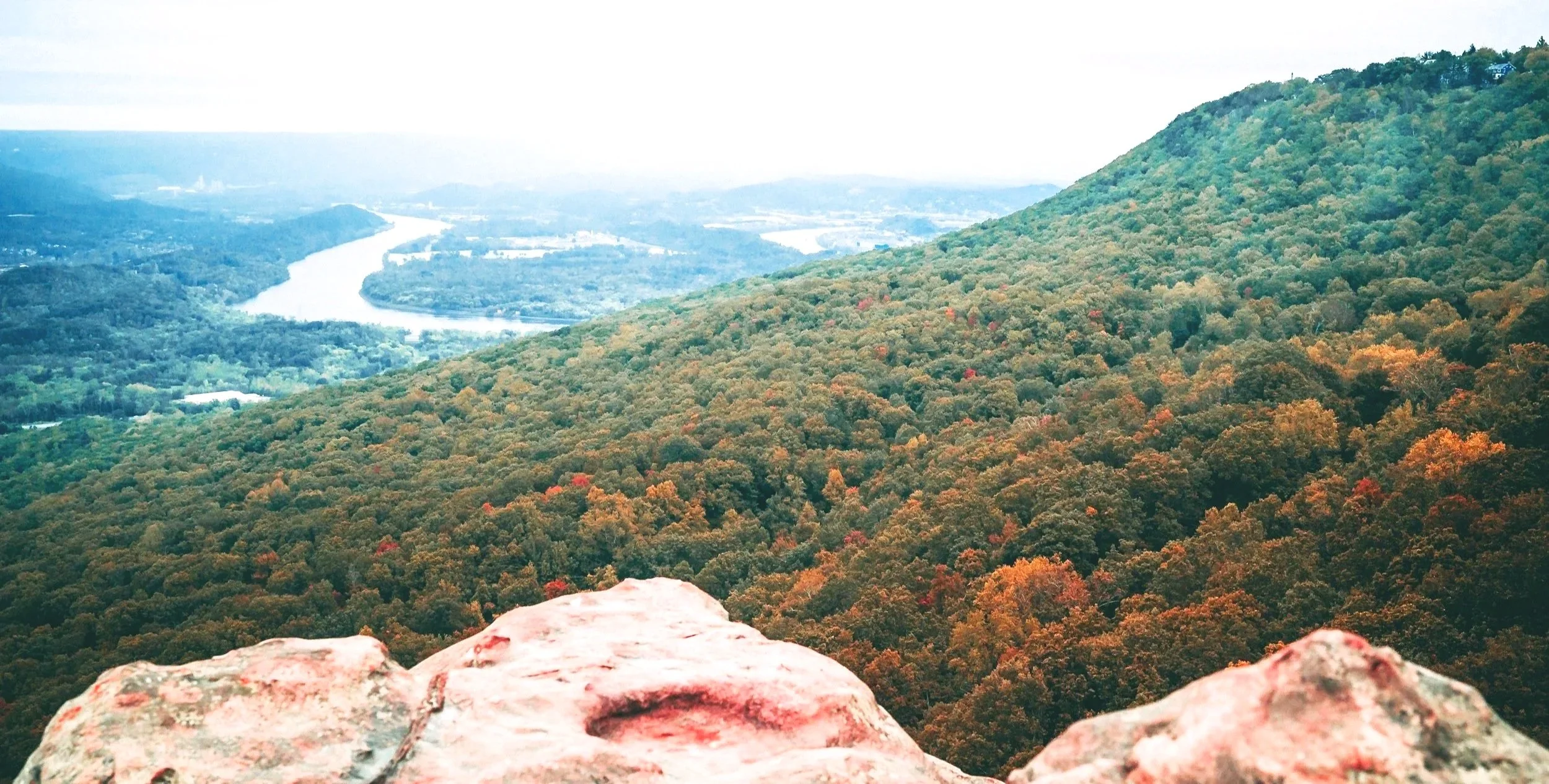 Scenic view of the Tennessee river winding through the Tennessee Valley with forested hills in autumn colors, seen from a rocky vantage point.