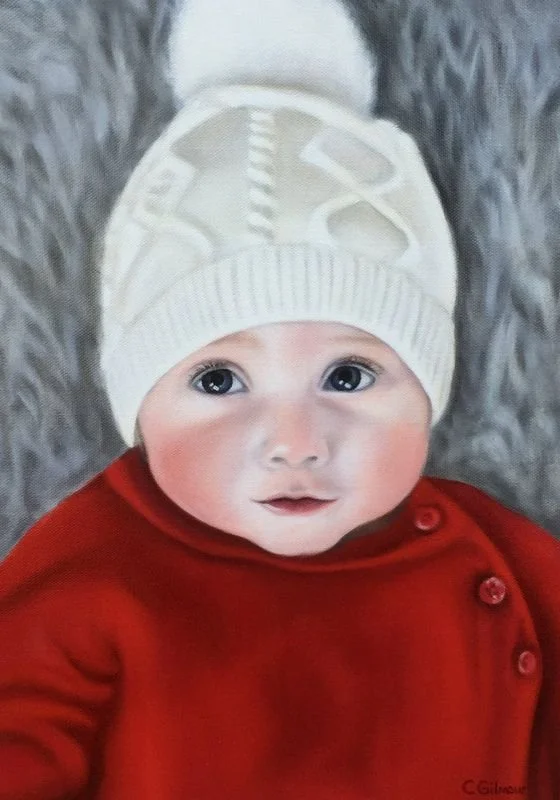 A baby wearing a white knit hat and a red coat, lying on a gray fuzzy blanket.