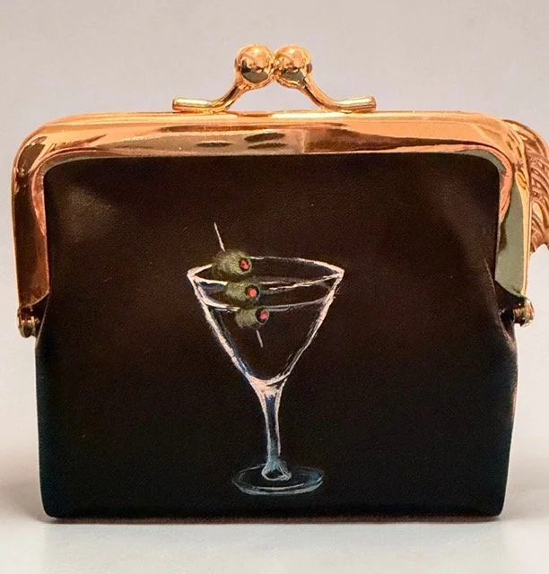 A black purse with a painted illustration of a martini glass containing two green olives with red pimentos and a cocktail pick.