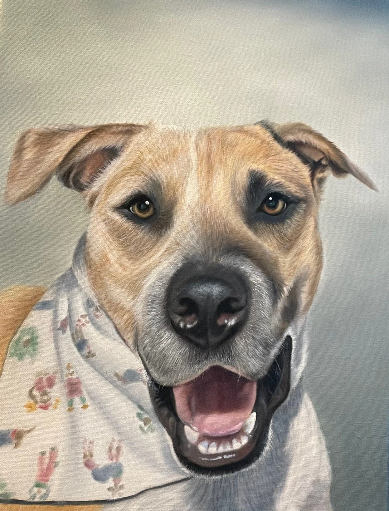 Close-up of a happy, smiling dog with a light brown and black coat, wearing a floral bandana.