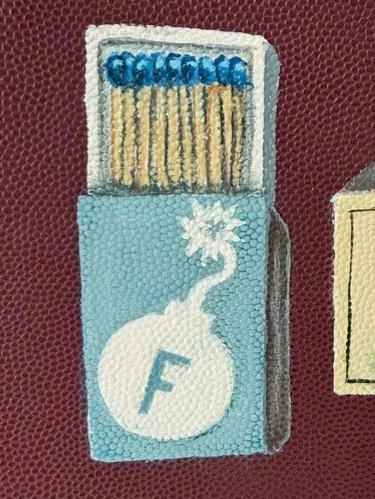 Illustration of a pack of matches with a blue label and a white chemist's symbol on the front, set against a maroon textured background.
