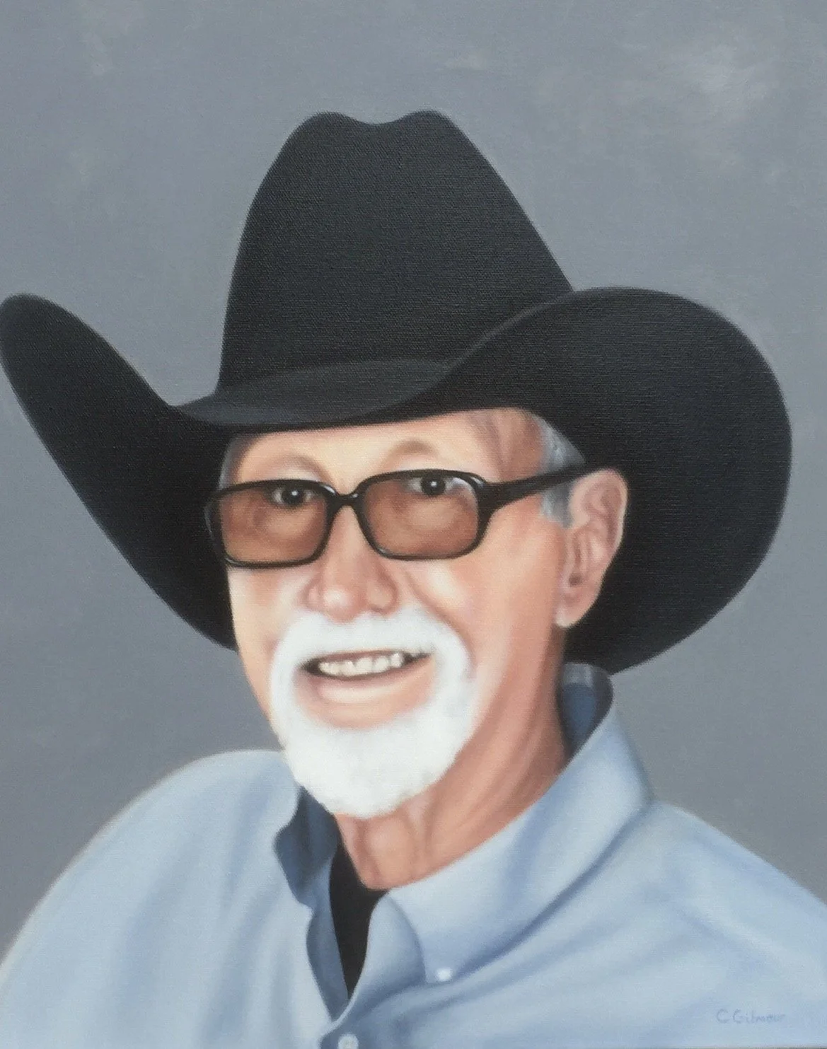 Portrait of an elderly man with glasses, a white goatee, wearing a black cowboy hat and a light blue collared shirt, smiling against a gray background.