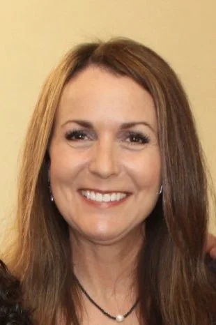 Close-up of a woman with long brown hair smiling against a yellow background.
