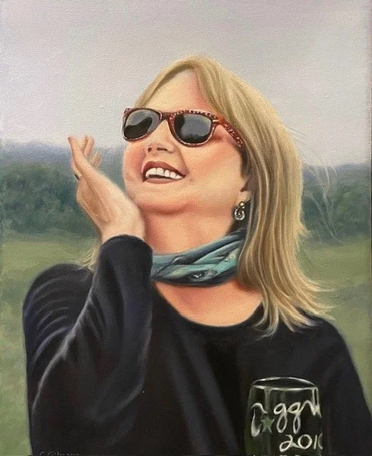 A woman wearing sunglasses and a scarf, smiling outdoors, holding a mug.