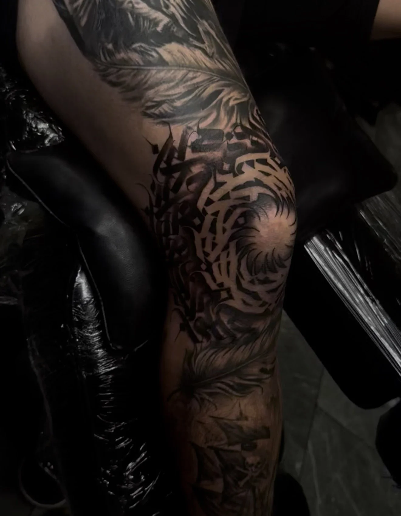 A tattooed person's arm resting on a black armrest of a tattoo chair.