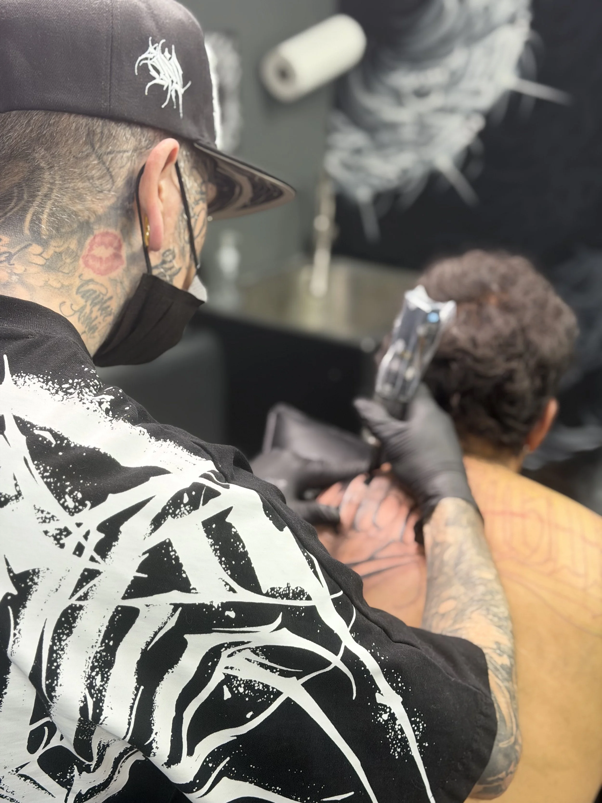 Tattooed man with glasses and face mask getting a tattoo on his arm in a tattoo shop