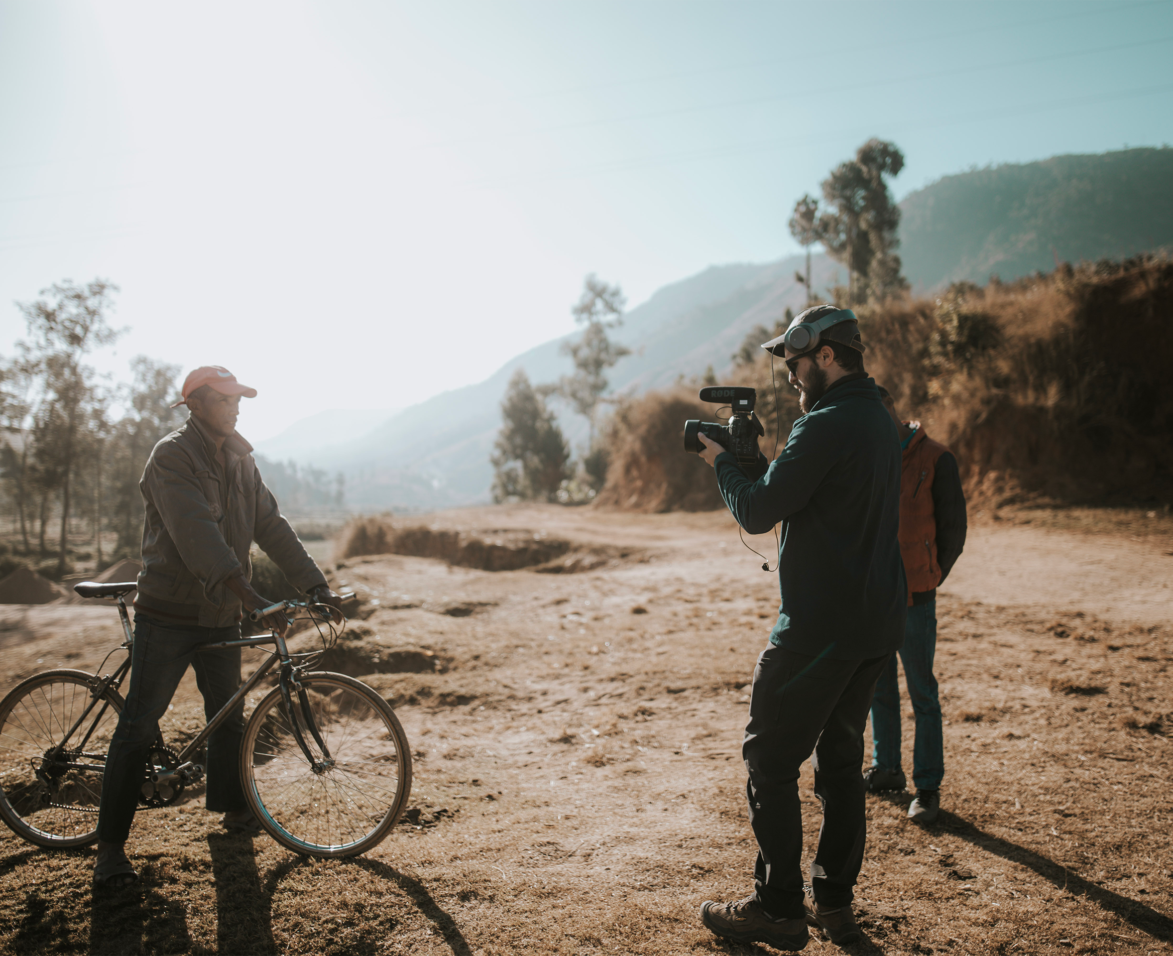 Grayson Zaragoza of North Sky Productions filming on location during international production, documenting local subject with bicycle in rural landscape