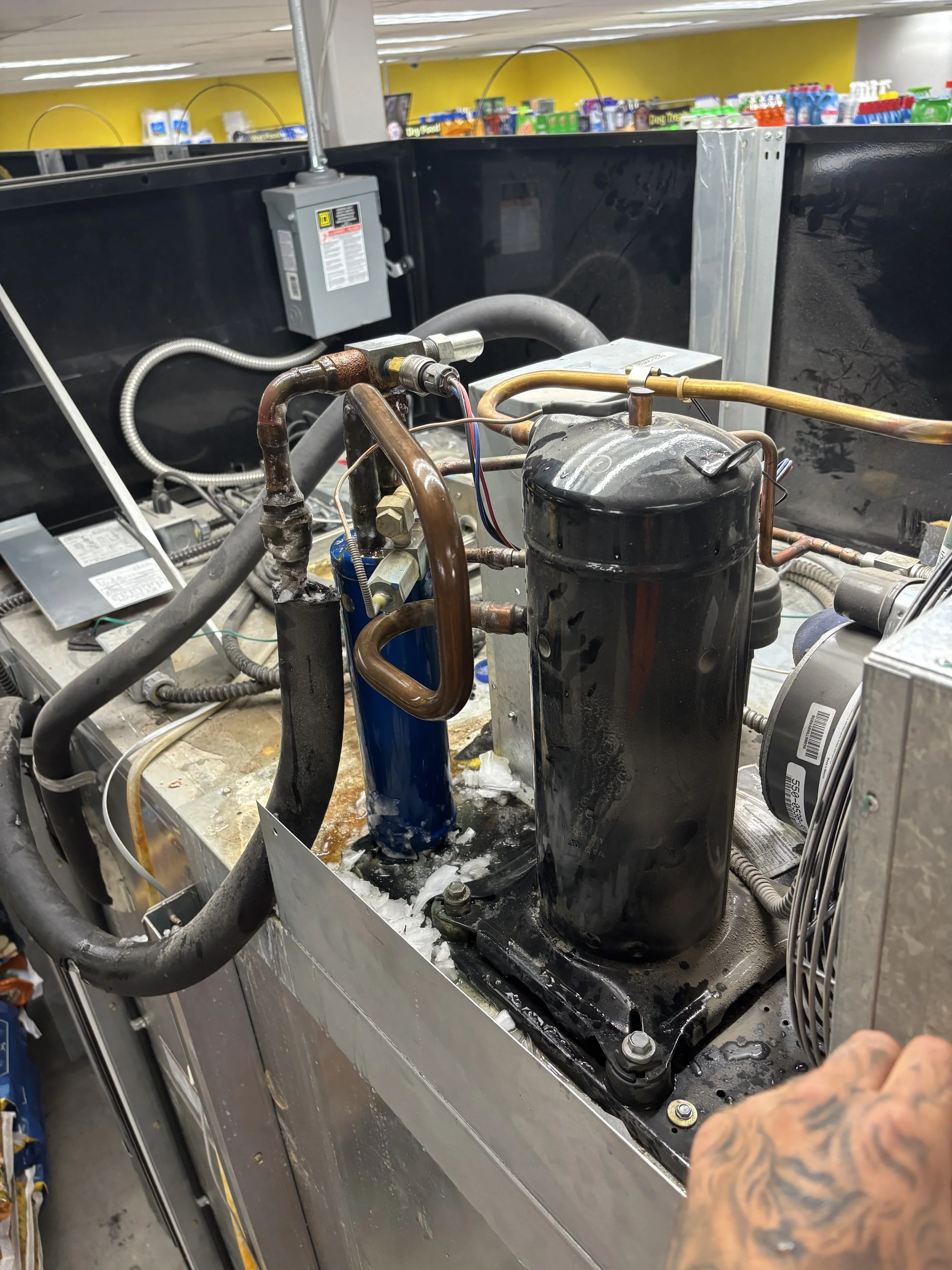 Close-up of a refrigerator compressor unit with copper and steel pipes, some of which are frosted over, situated inside an appliance repair shop.