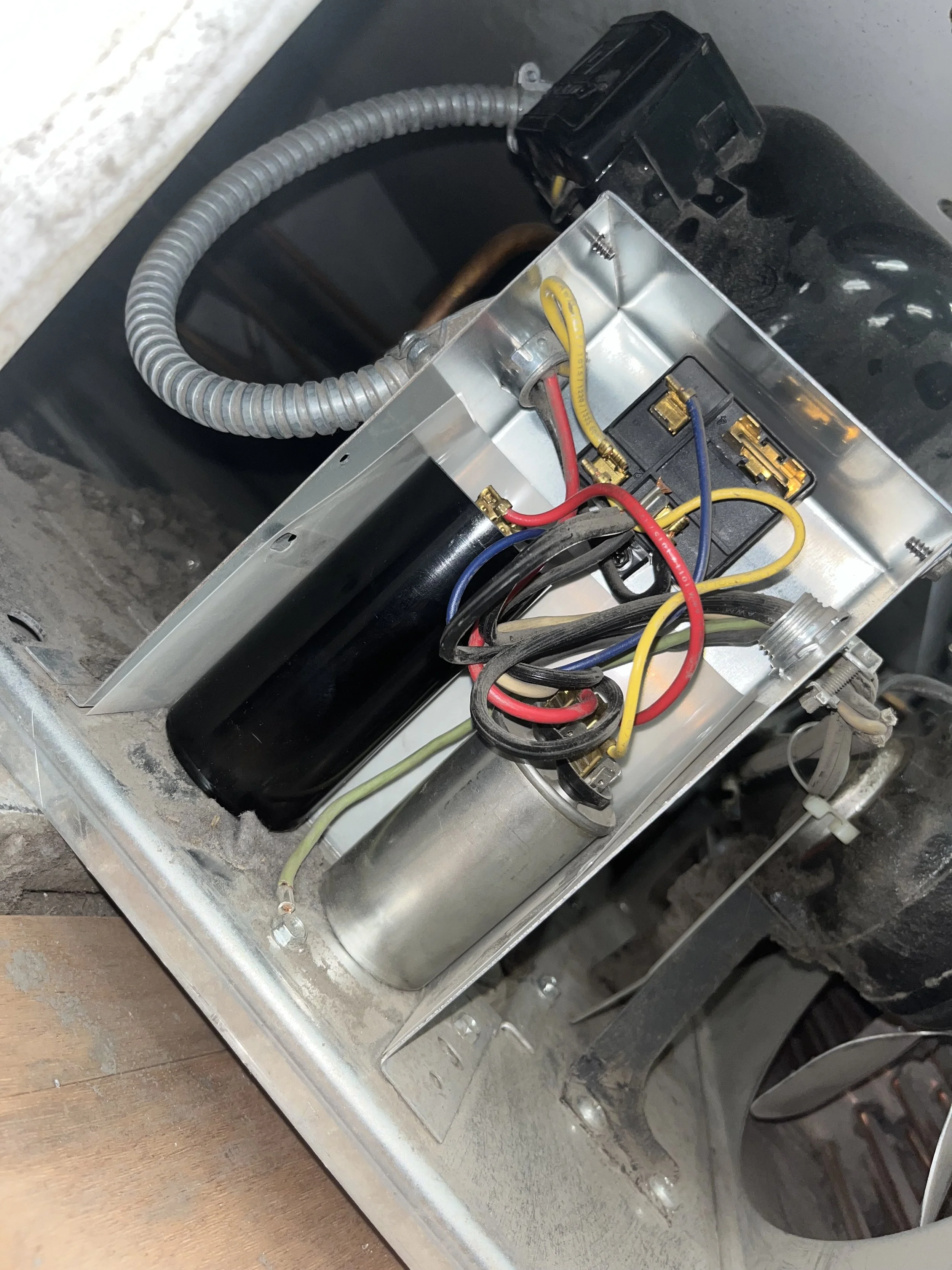 Open electronic device displaying internal components including wires, capacitors, and a black cylindrical component, with dust and dirt inside a metal casing.