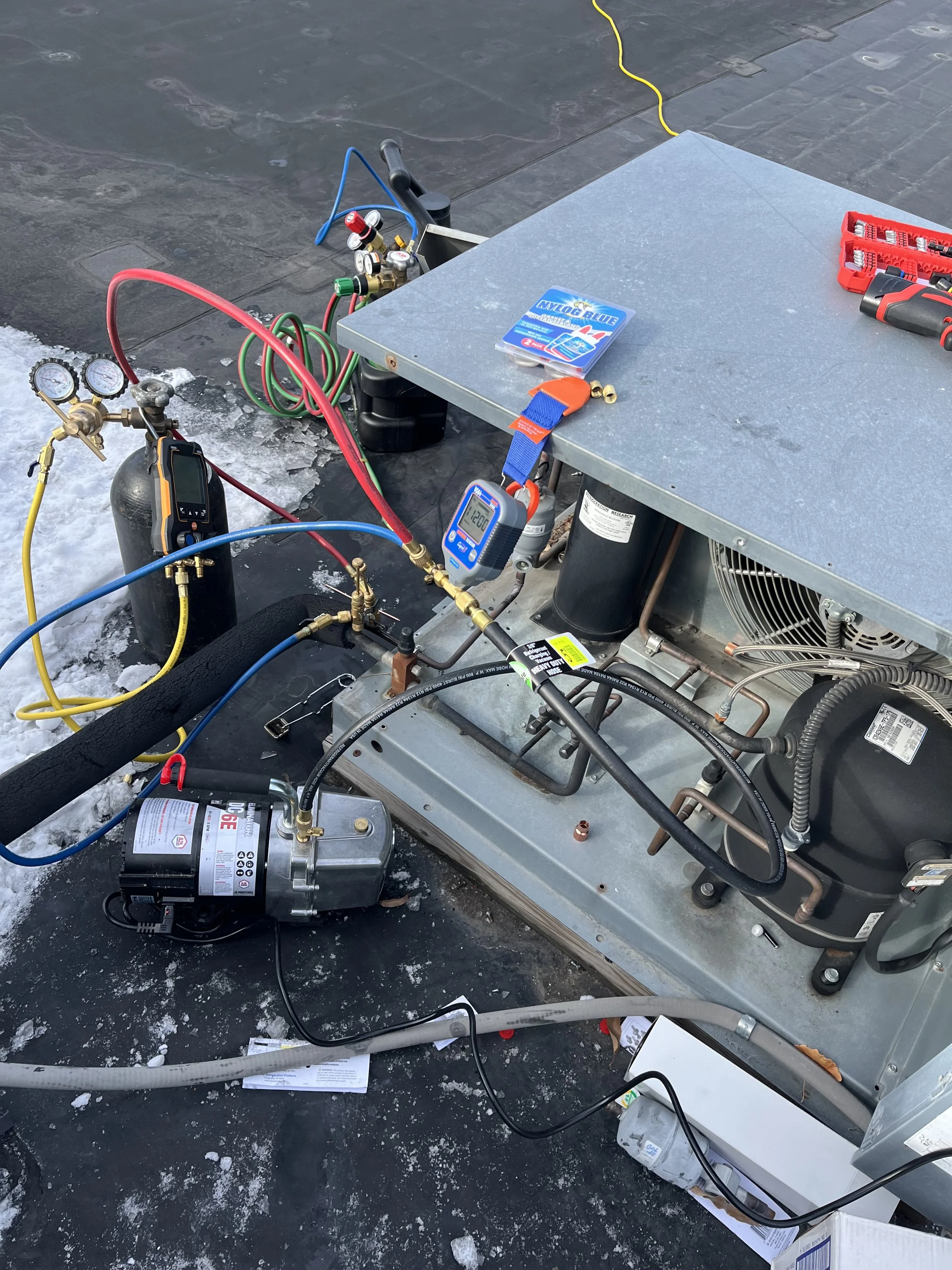 HVAC or refrigeration system with various gauges, hoses, and electronic components set up on a rooftop, including a compressor, digital controllers, and tools.