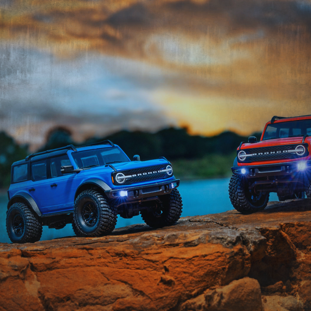 Two Traxxas RC Crawlers, Bronco off-road vehicles on rocky terrain outdoors during sunset with dramatic sky.