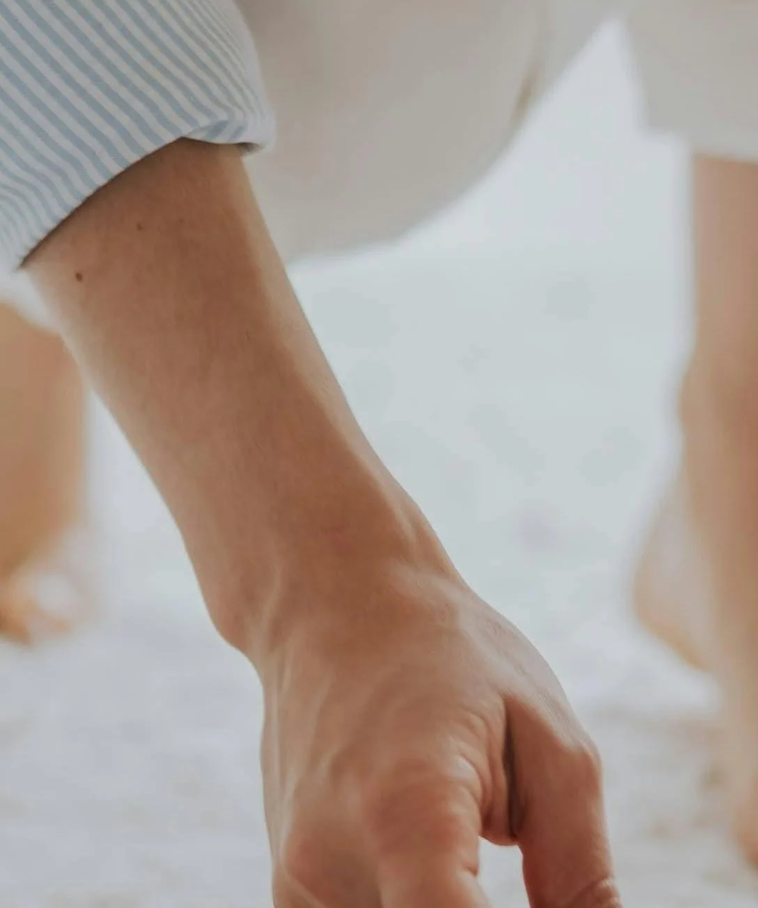 Close-up of a person's arm and hand reaching down, with a blurred background.