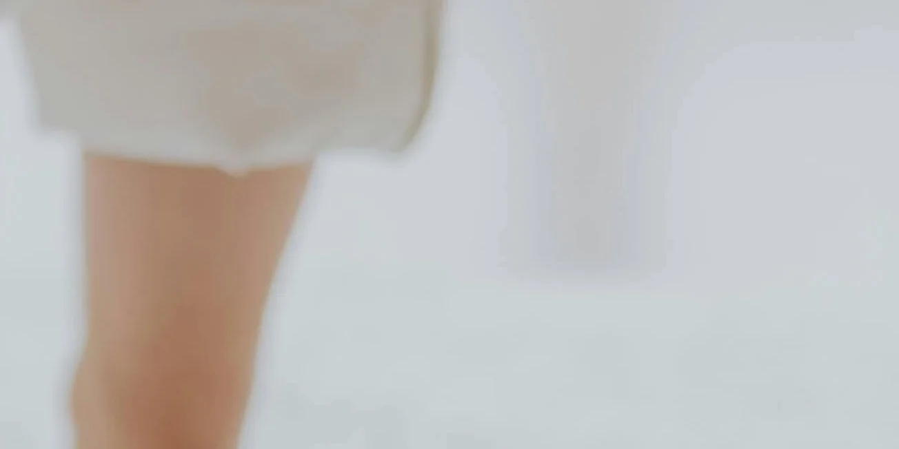 Close-up of a person's leg and part of a white garment against a light background.