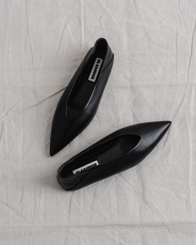 A pair of black pointed-toe high heels on a light-colored fabric surface.