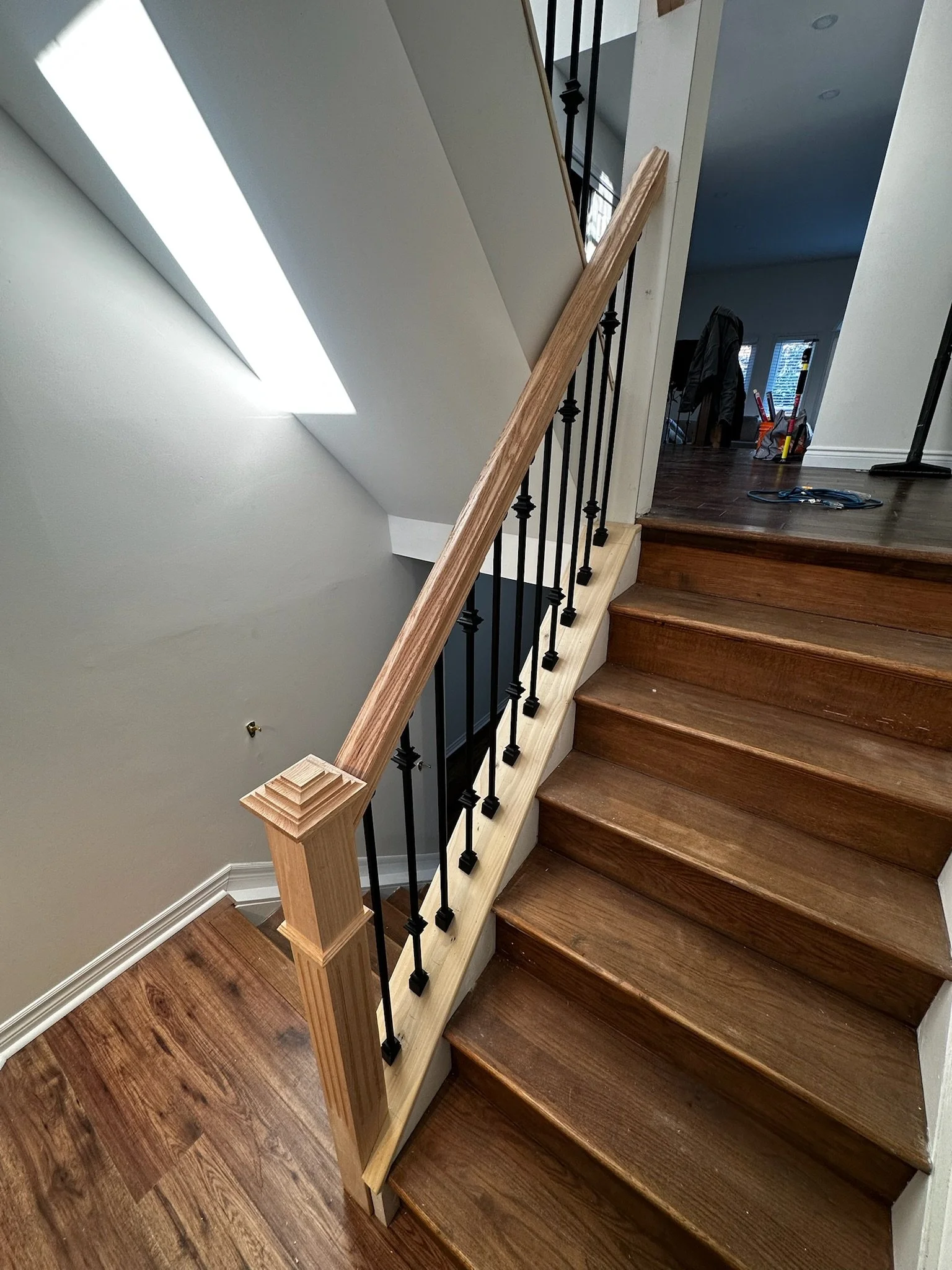 Interior of a house with a wooden staircase, black metal balustrade, replaced or renovated handrail, and hardwood flooring.