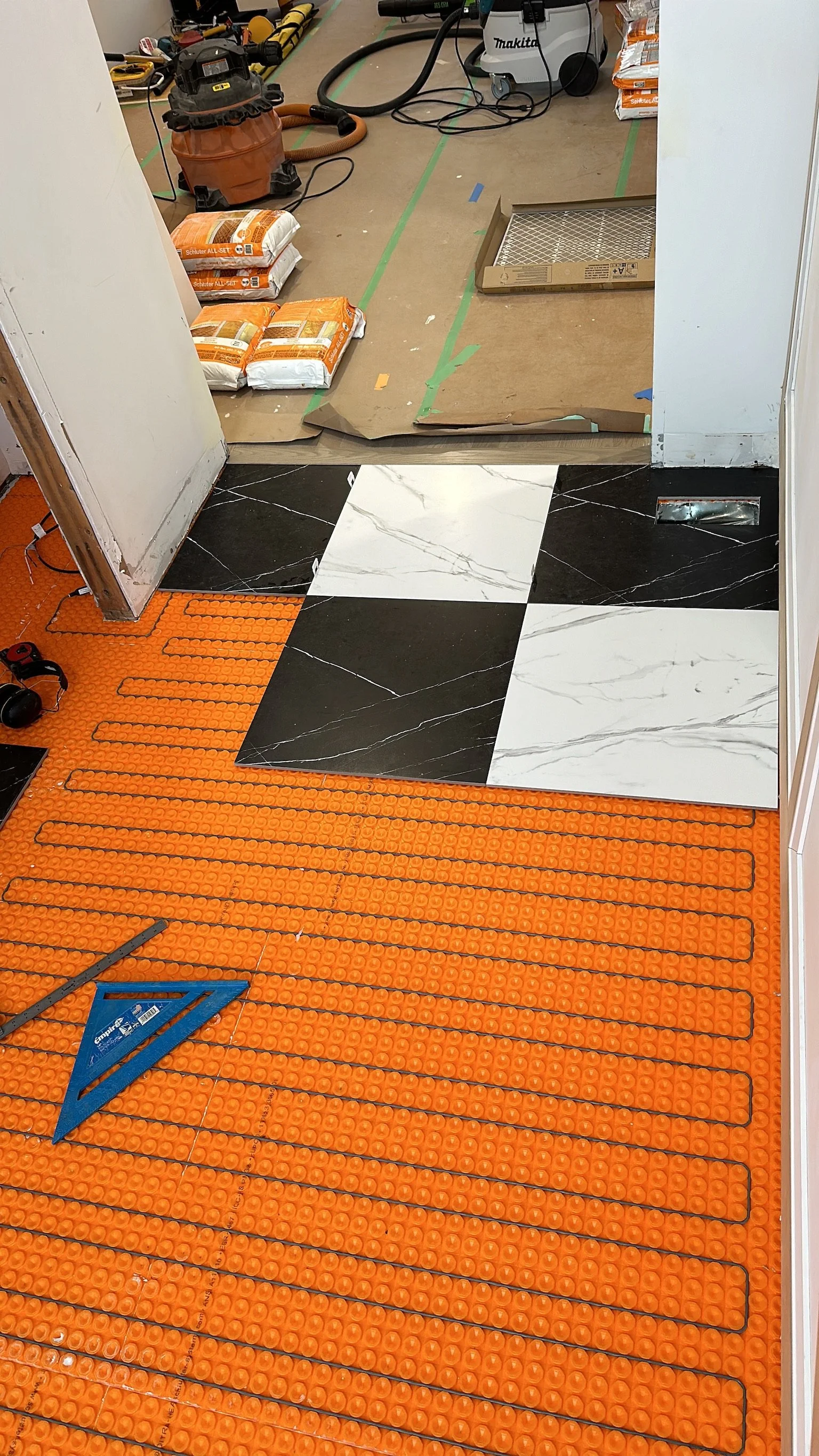 Floor being installed in a room, with orange heating cable floor mat, and black and white marble-like tiles partially laid. Even and well-designed subfloor with perfectly measured tiles so there is no waste of materials.