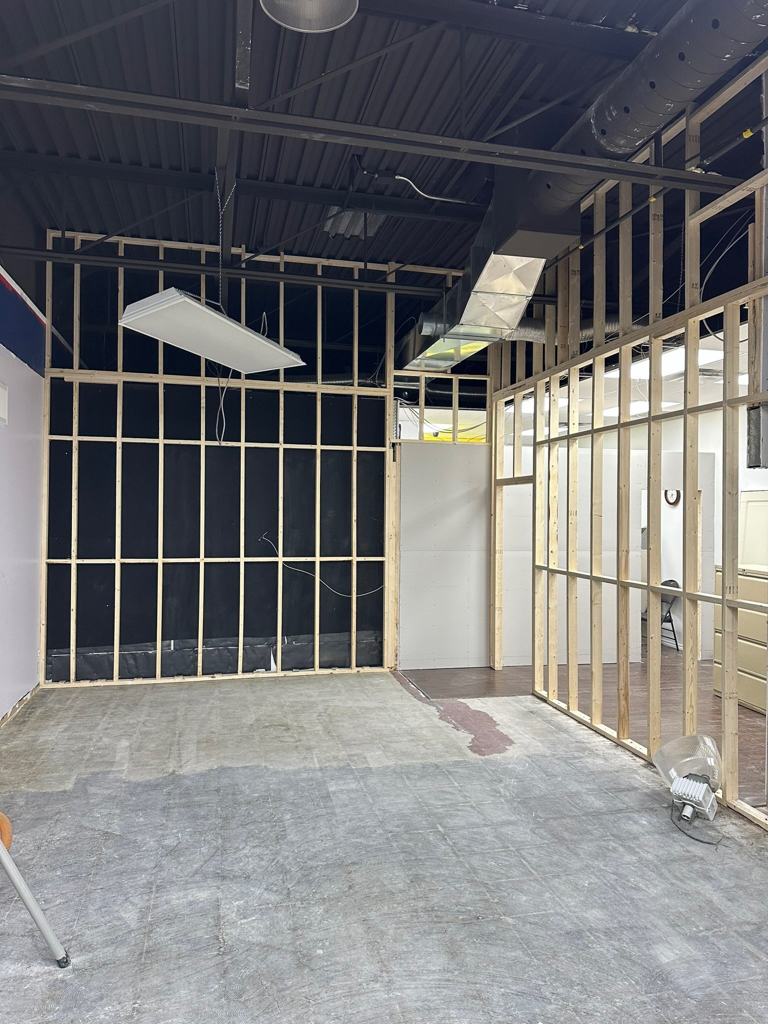 Perfectly measured wooden framing and overhead lighting, floor covered with gray concrete, ductwork and electrical wiring neat and visible on ceiling.