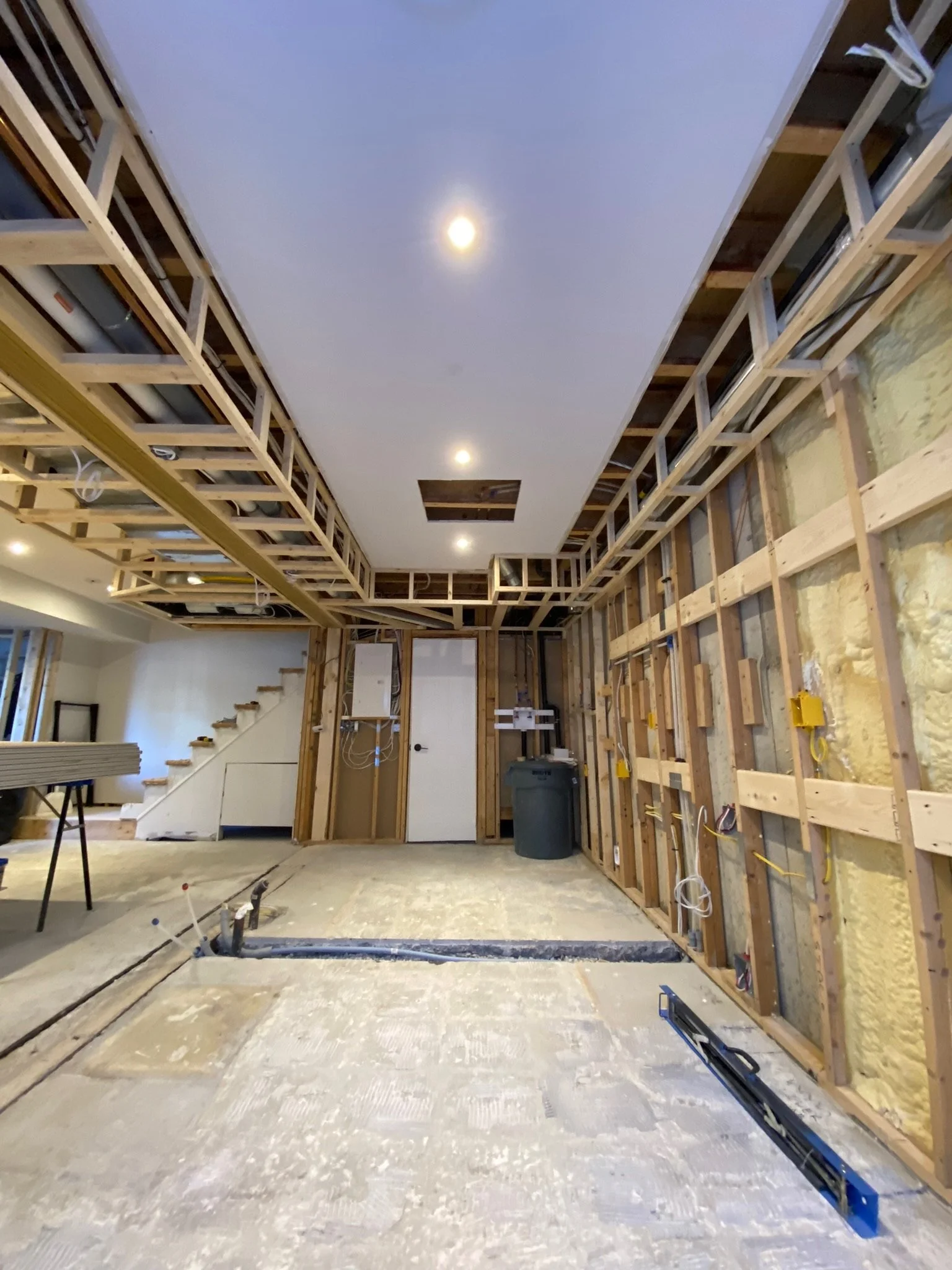 Interior view of a house under construction, with meticulously measured wooden framing, and a partially finished ceiling with lighting. It's a very neat and organized construction site for a sturdy and dry basement.