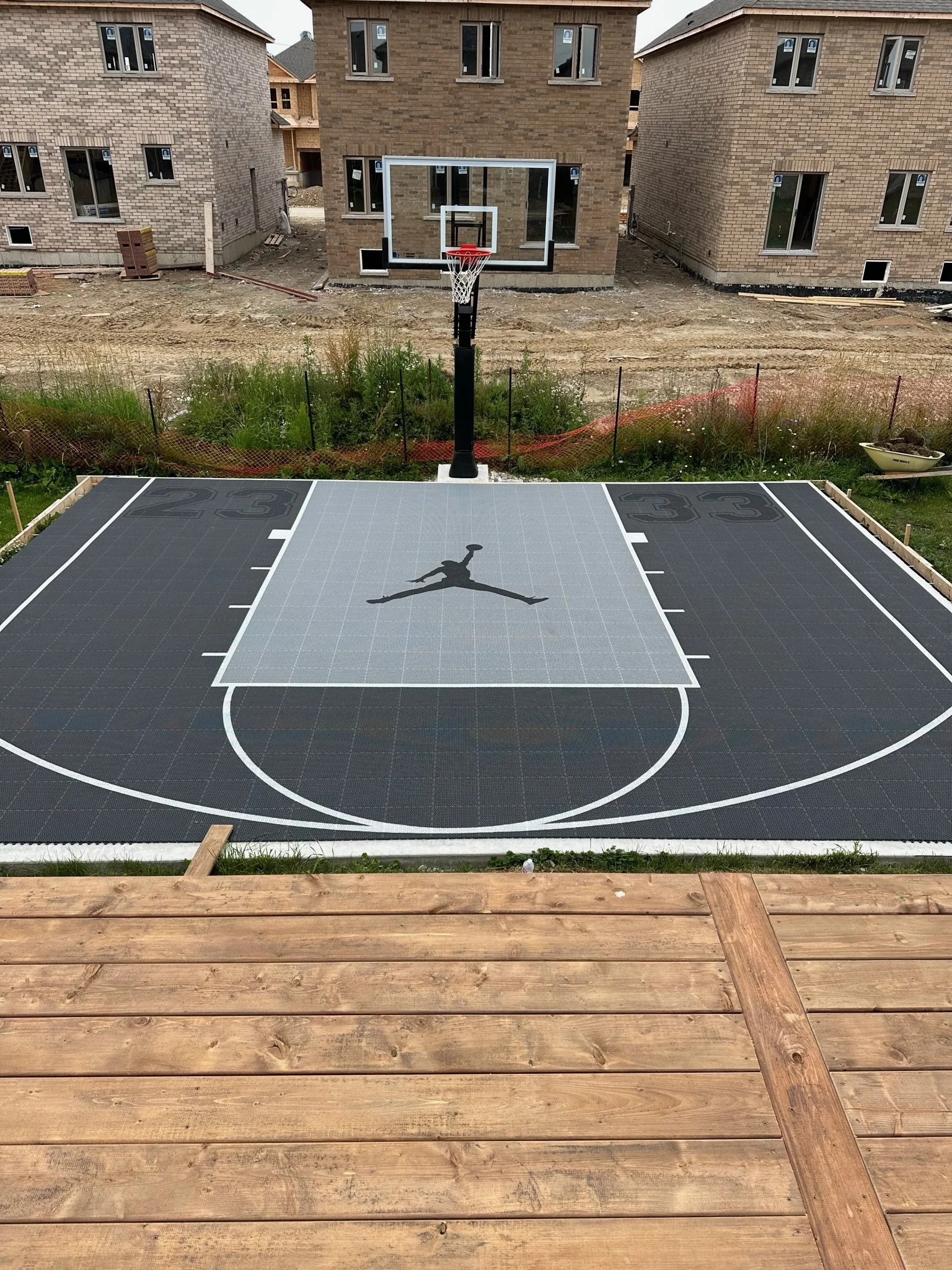 A newly constructed custom outdoor basketball court with black and gray surface, made for all-seasons with a basketball hoop.
