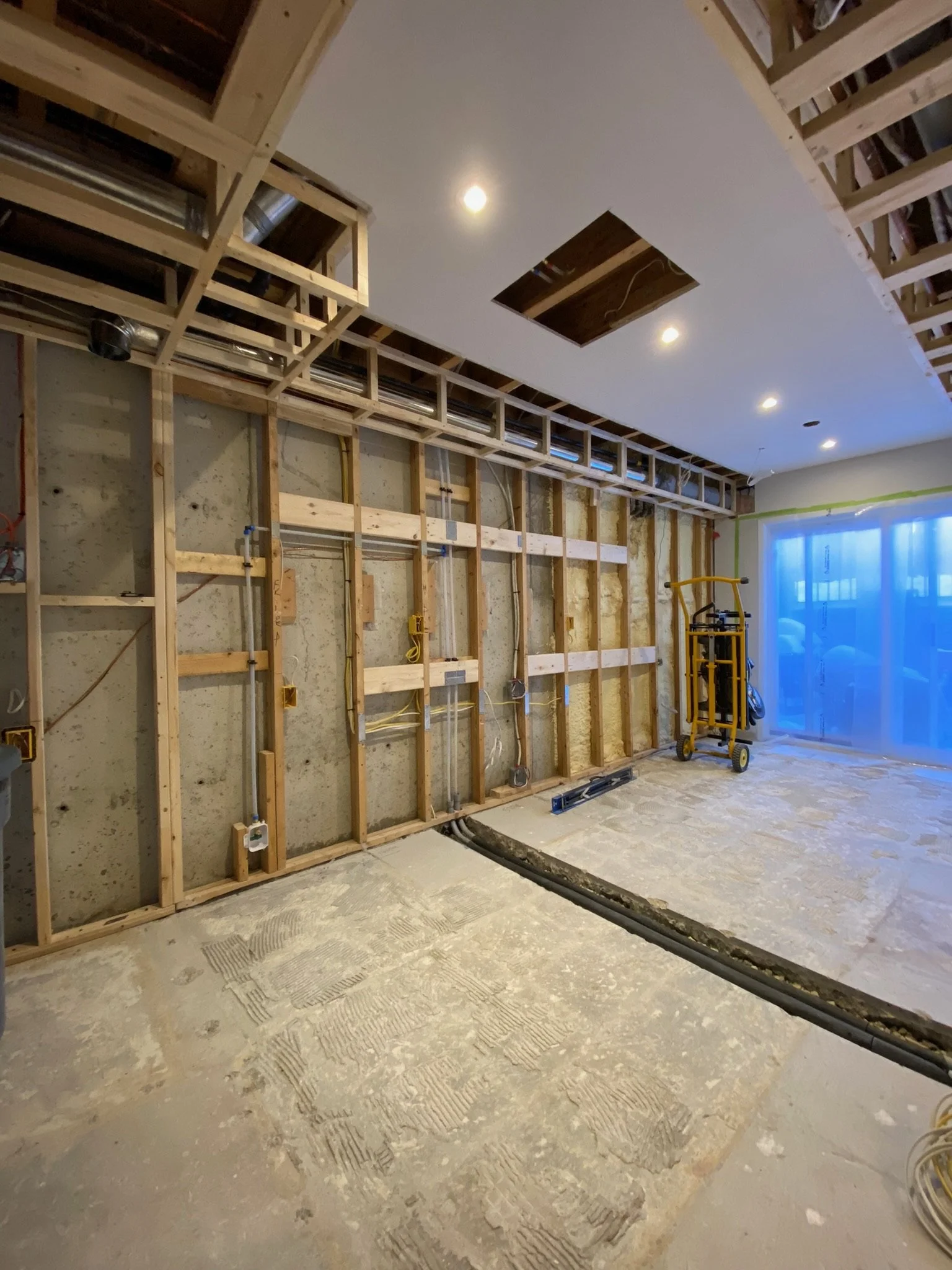 Interior of a room under organized construction, showing exposed wooden framing on the walls and ceiling, flooring, and construction equipment. Skilled work of an experienced construction worker.