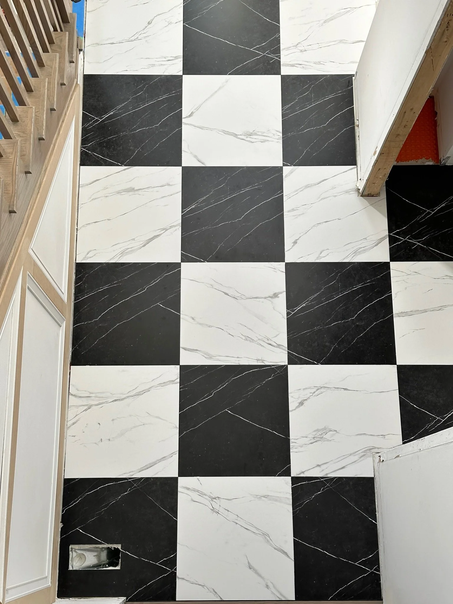 A black and white checkered marble-tile floor with a stair railing on the left and a door frame on the right.