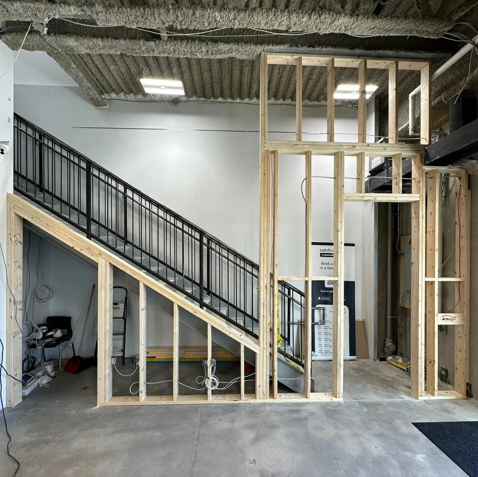 Interior of a building under construction, showing meticulous wooden framing for walls and staircase, electrical wiring to code and well-organized construction tools on the floor.