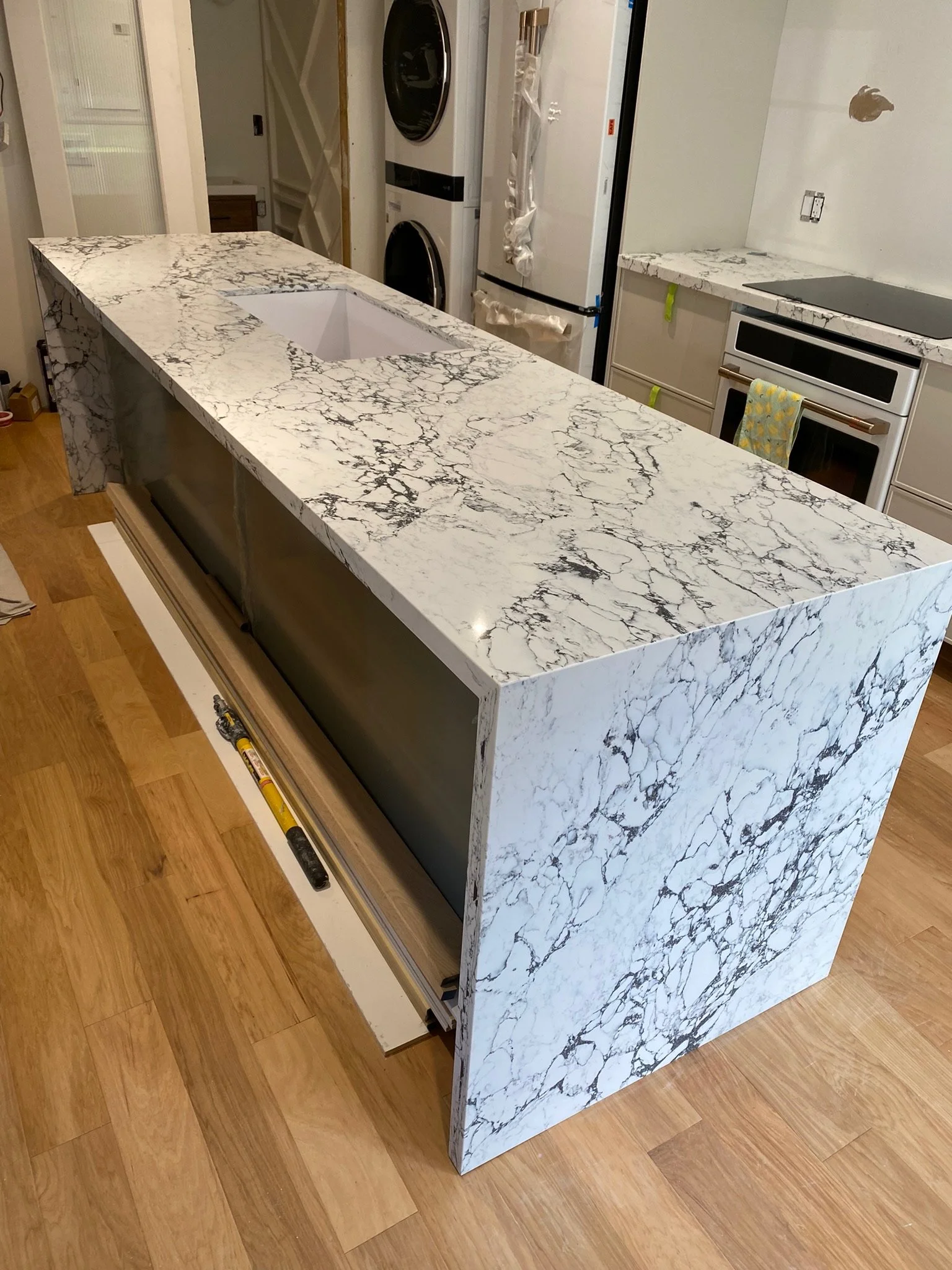 A kitchen island with a marble pattern countertop, featuring a hole for a sink, and a wooden base on a hardwood floor.