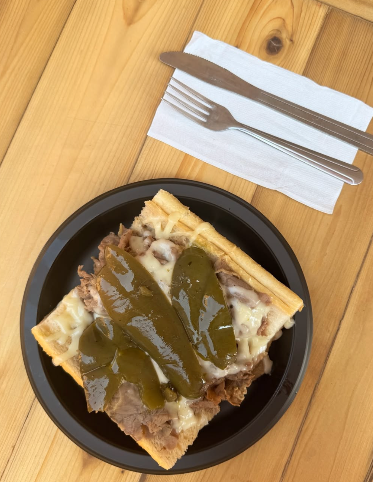 Close-up of a slice of Italian beef on a black plate, on a wooden table with a fork and knife on a napkin.
