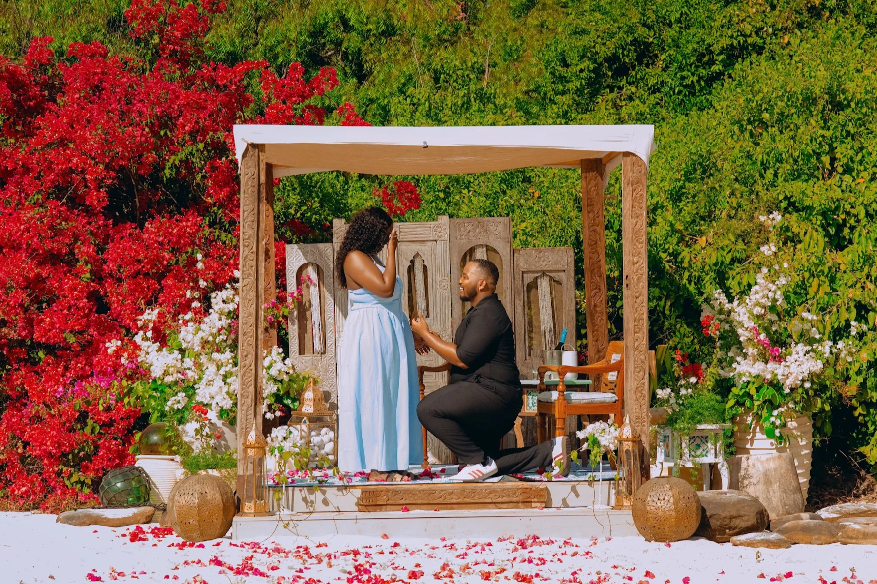 A couple proposed marriage during a colorful outdoor ceremony surrounded by red, white, and pink flowers and greenery.